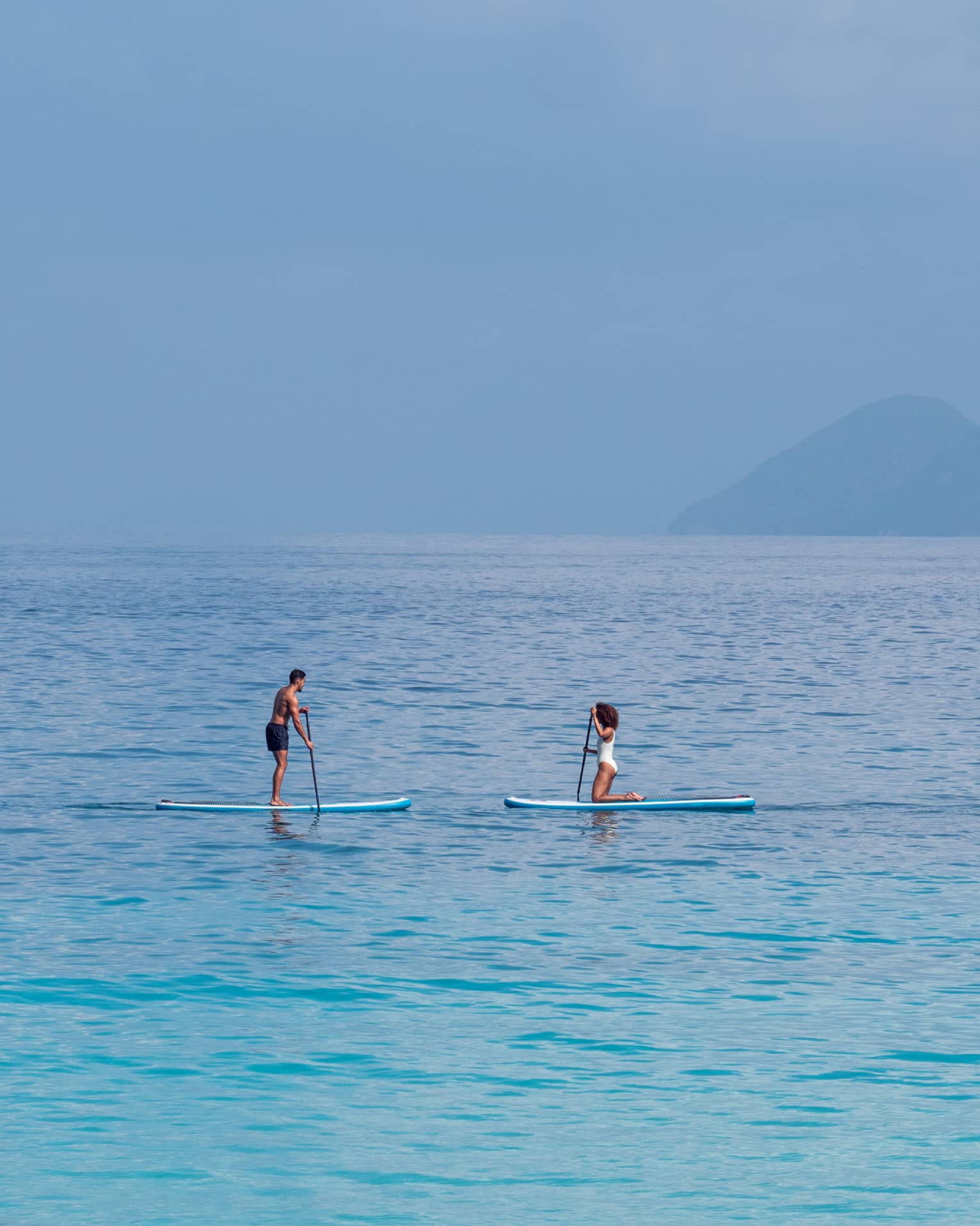 Man and woman paddle board on the open ocean, mountains visible through the fog