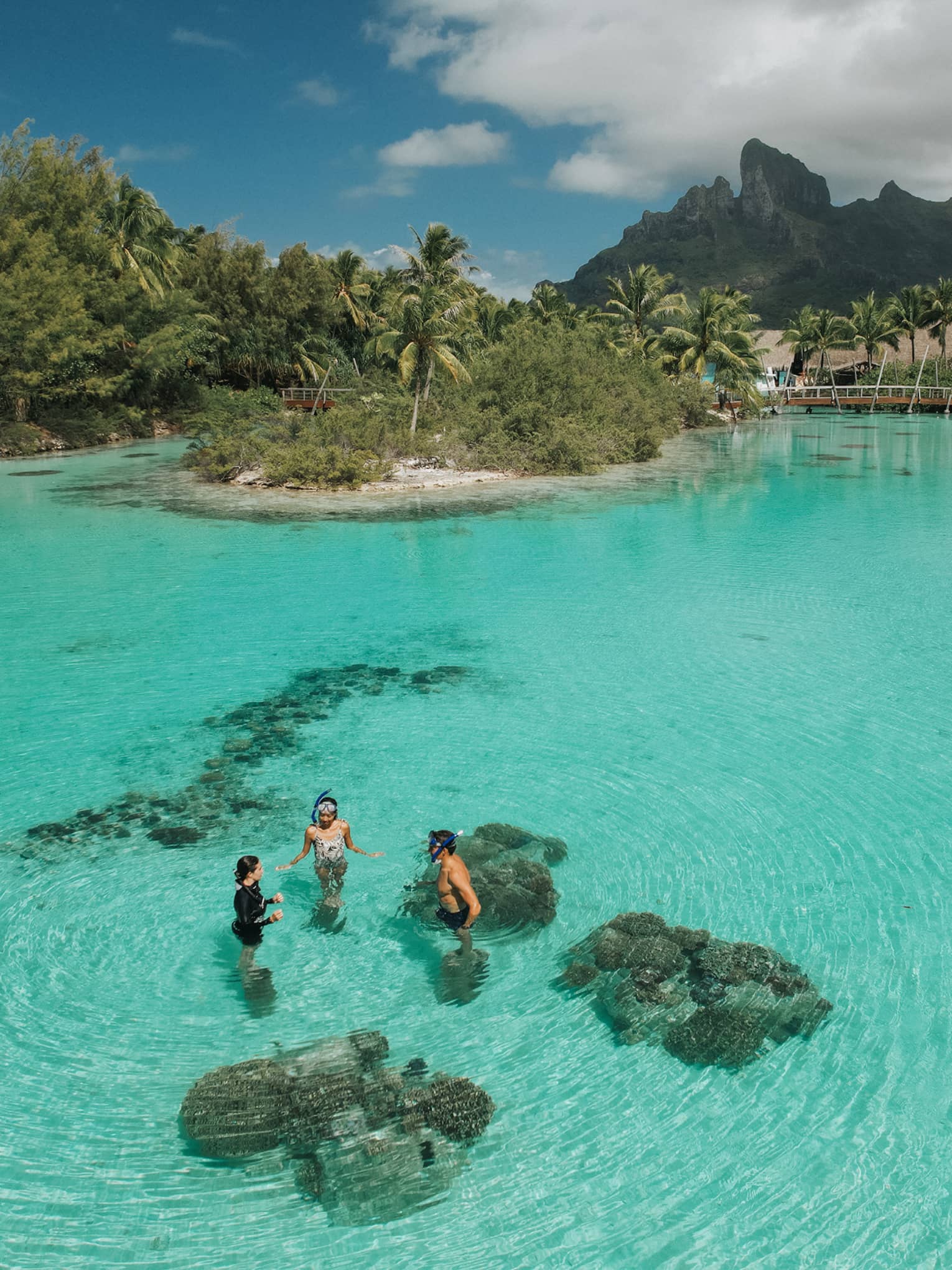 Aerial view of three guests standing in the clear turquoise water of the lagoon at the Dive Centre