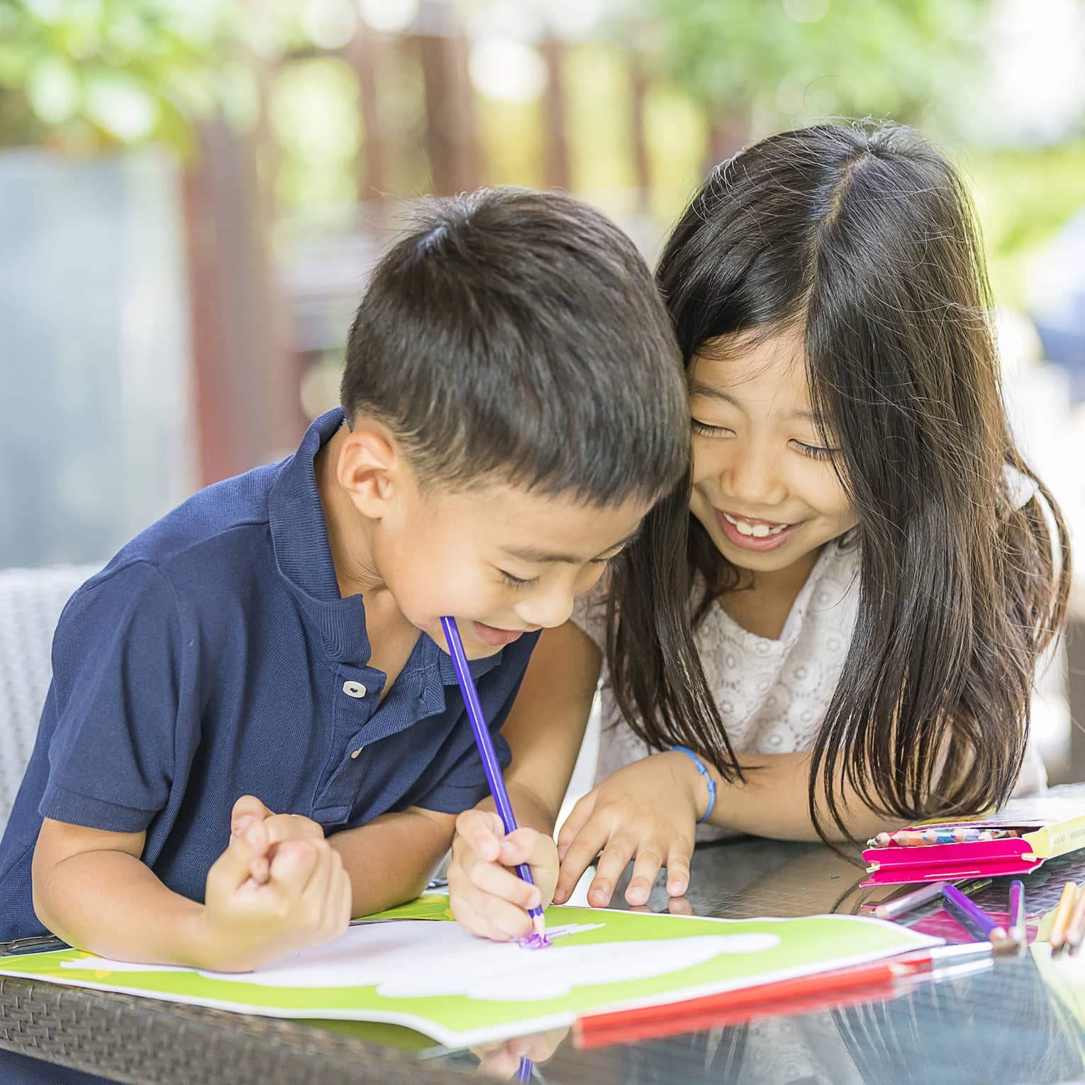 Smiling young boy and girl colouring in book with crayon
