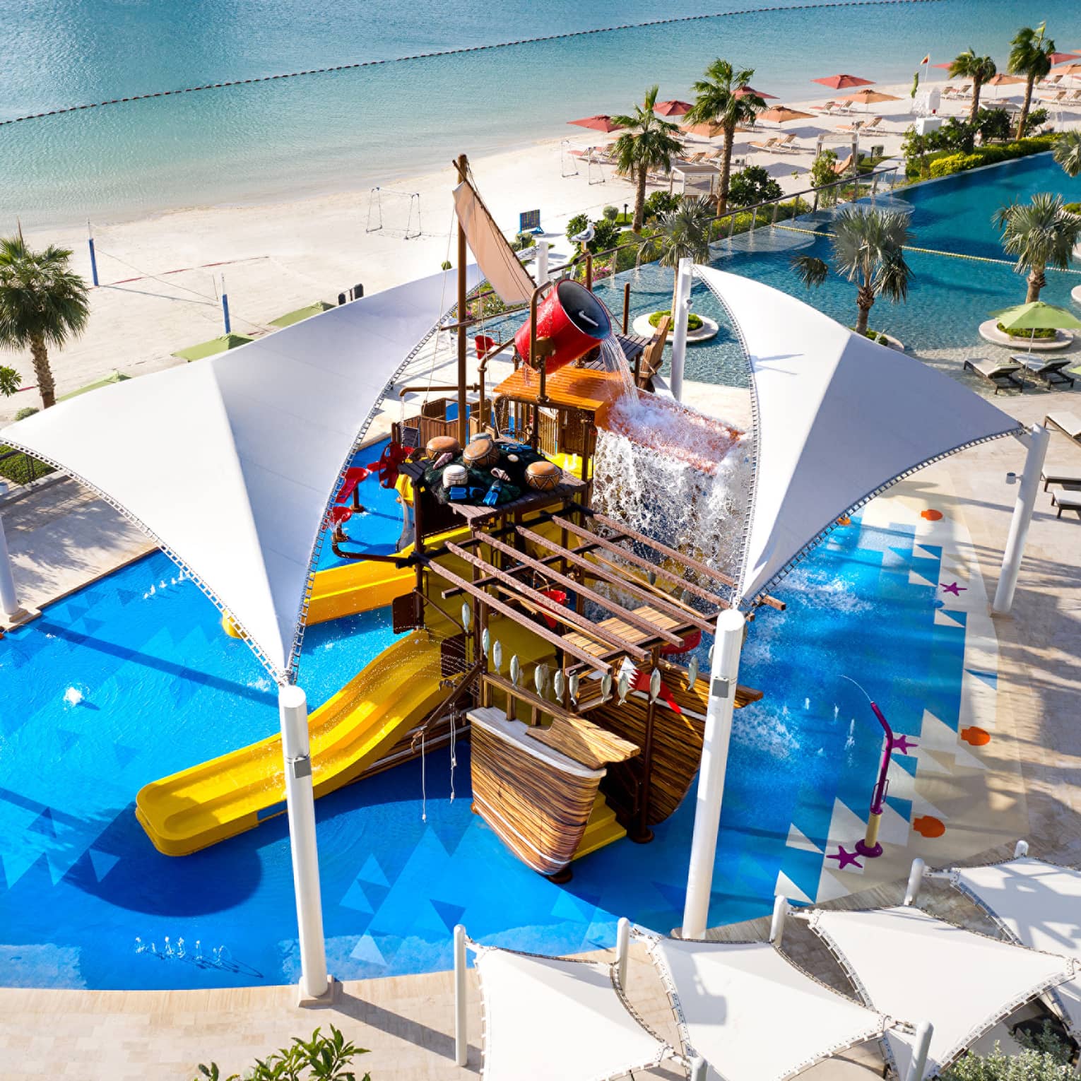 A large orange waterslide built into a faux pirate ship descending into a crystal blue pool of water.