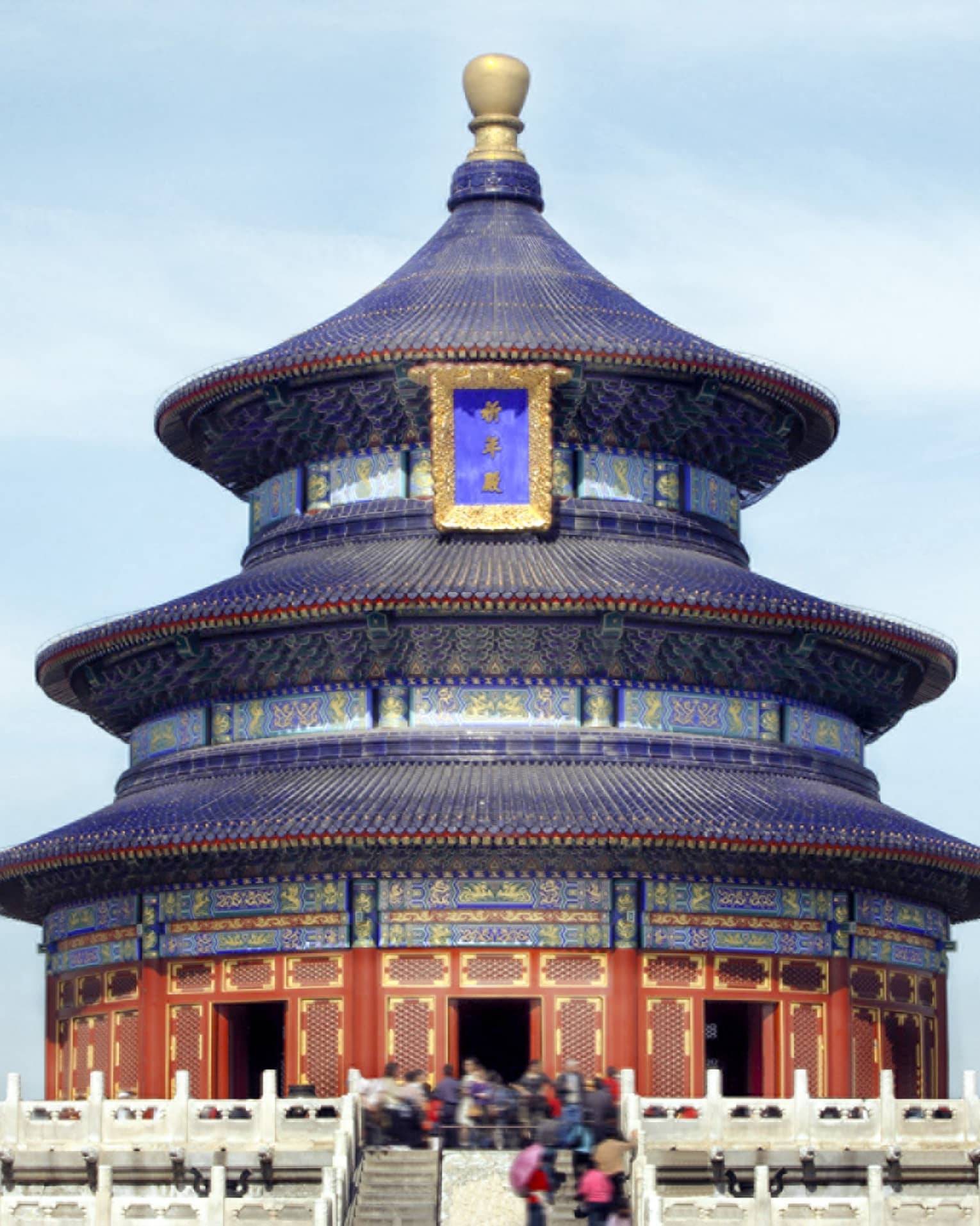 A close-up of a gilded, colourful triple-gabled circular temple bordered by a low, white balustrade against a clear blue sky.