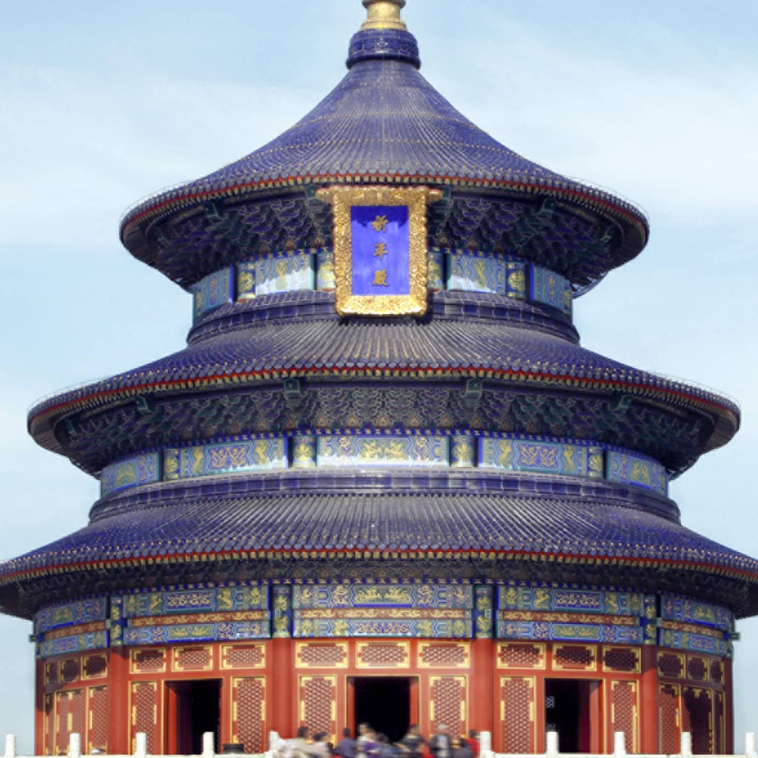 A close-up of a gilded, colourful triple-gabled circular temple bordered by a low, white balustrade against a clear blue sky.