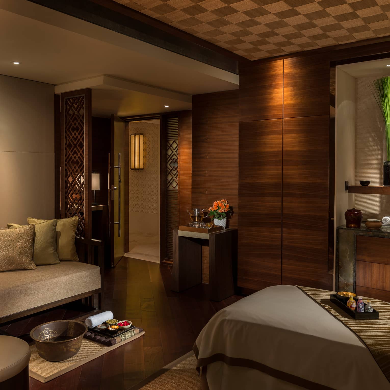 Spa treatment room with carved wood detail walls, bed and table with trays with oils