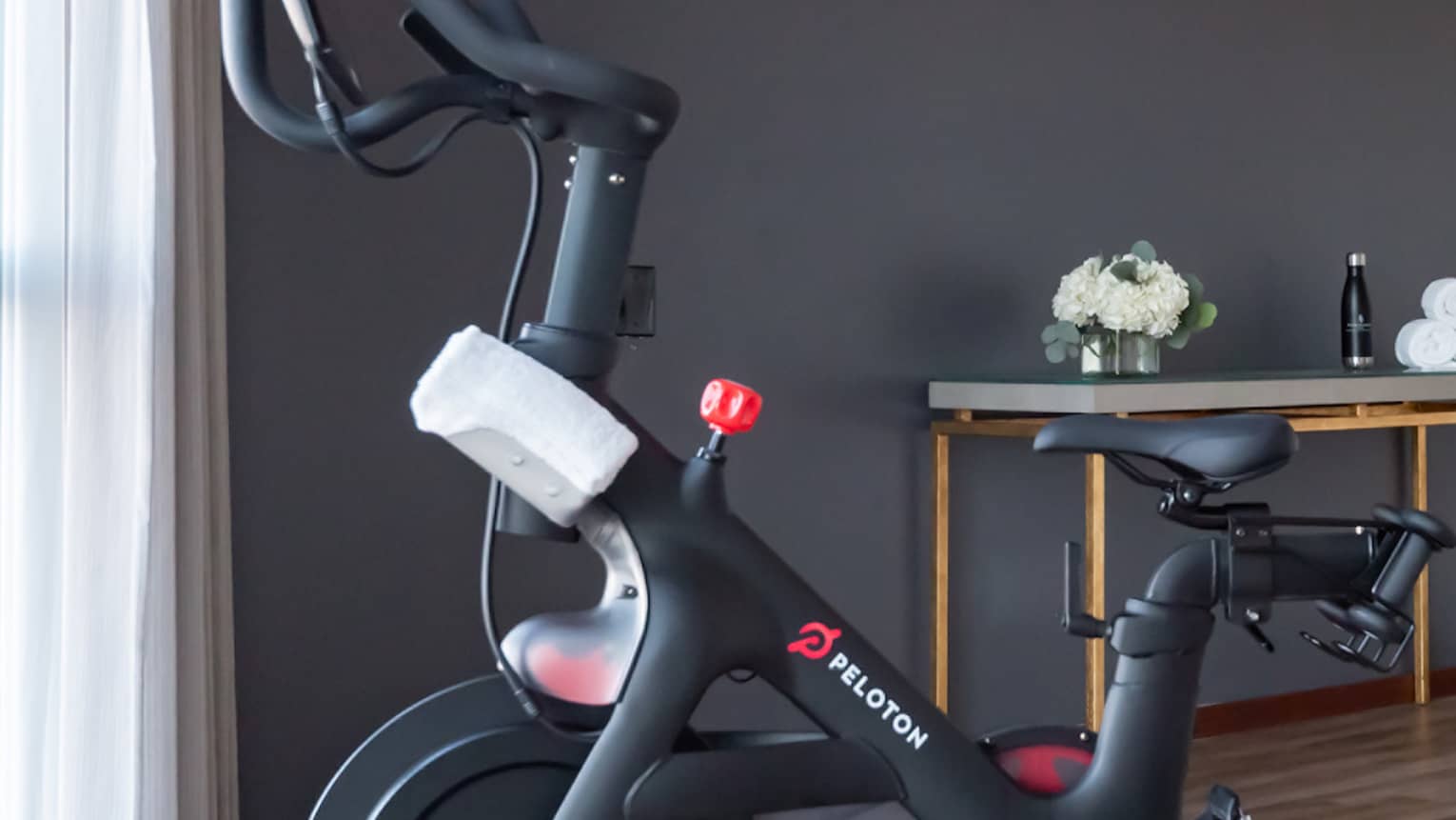 Peloton machine in a room with floor-to-ceiling windows on one wall.