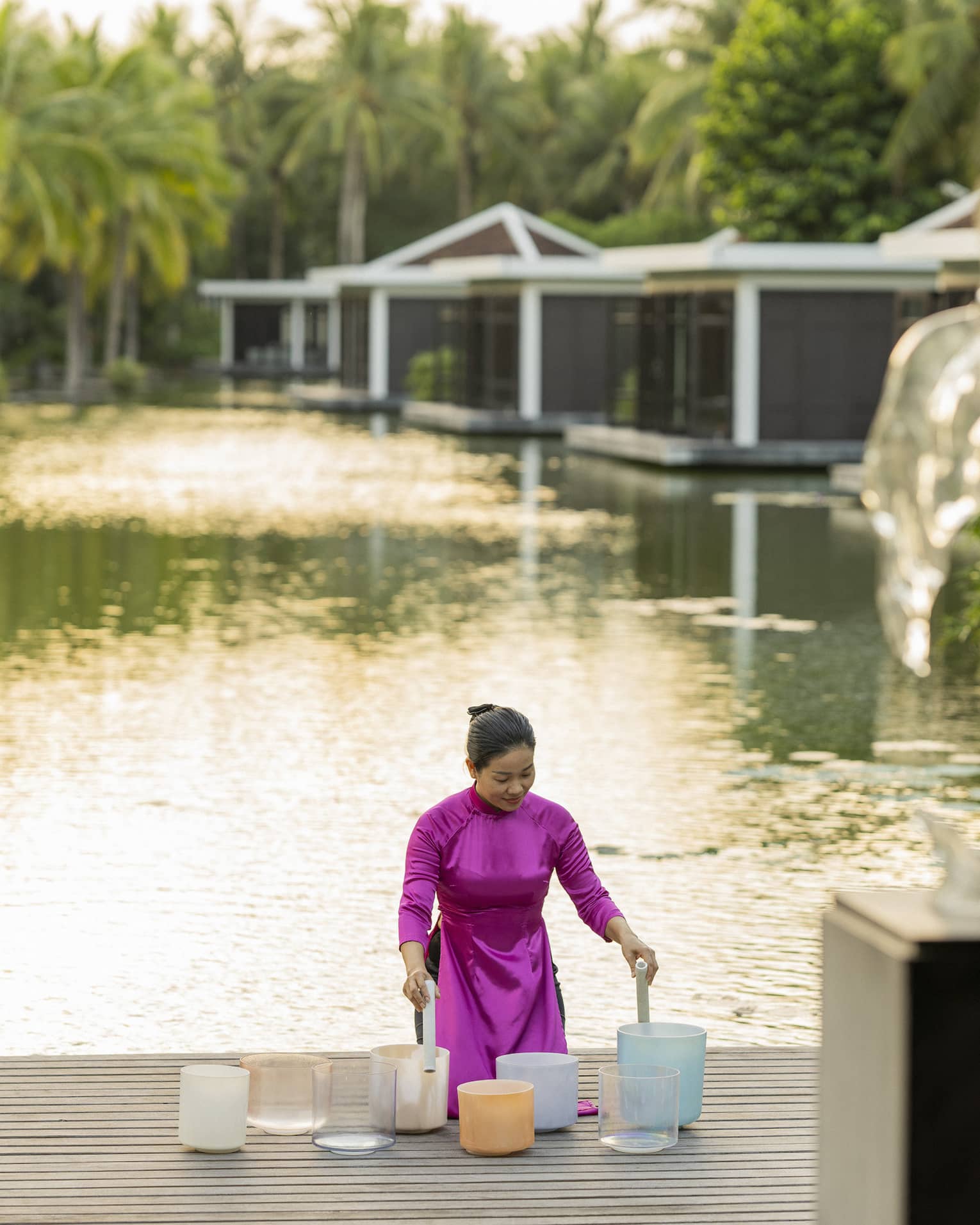 Woman plays crystal singing bowls on the dock of the lake