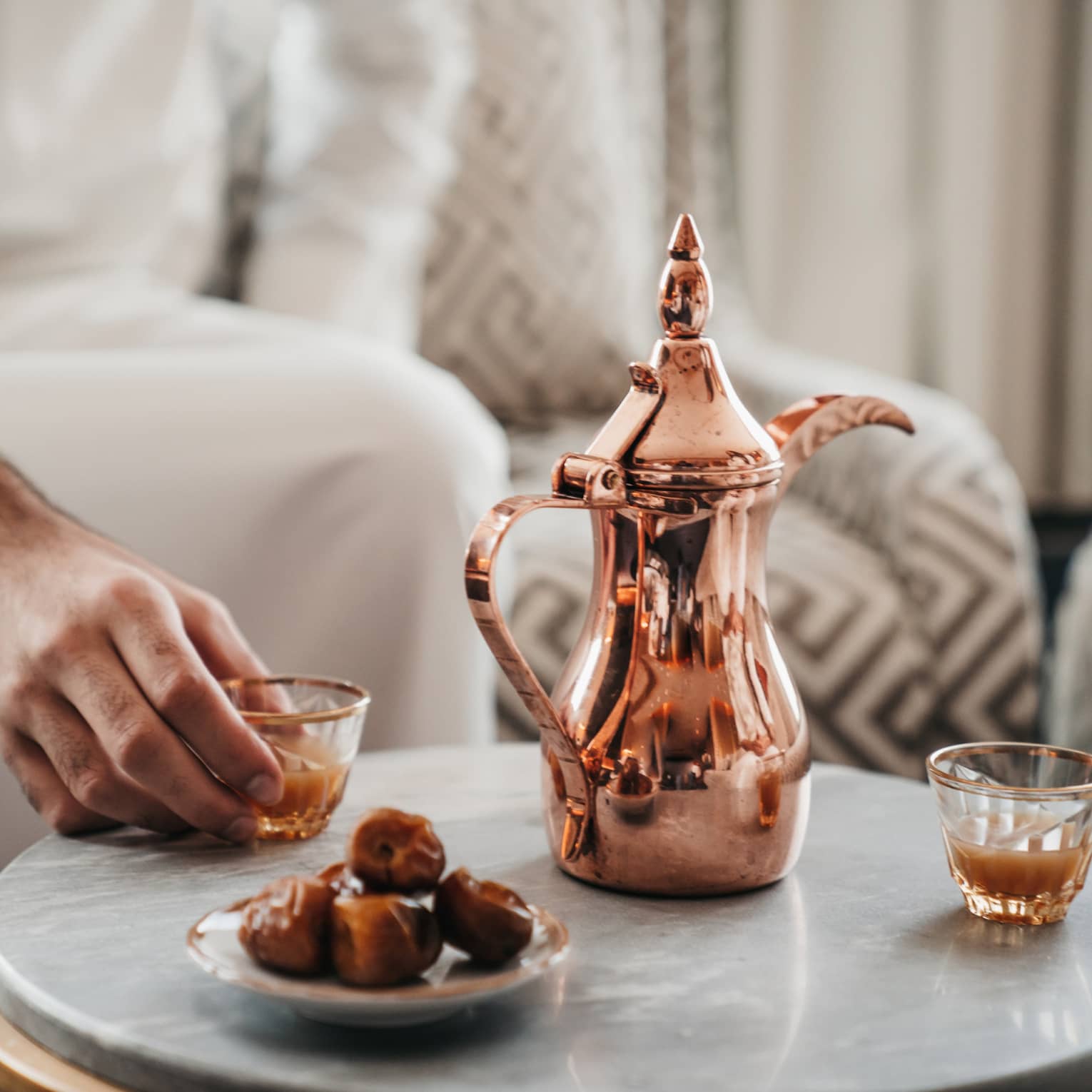Close up of copper coffee pot, some dried dates on a plate and two small gold-rimmed glasses
