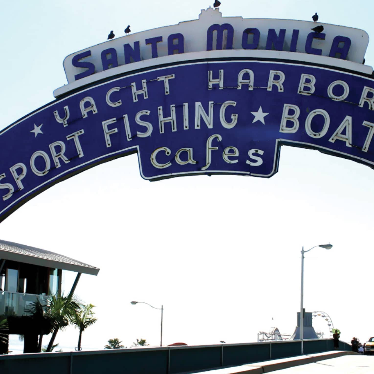 Navy blue Santa Monica sign on a pier, with people walking along the pier.
