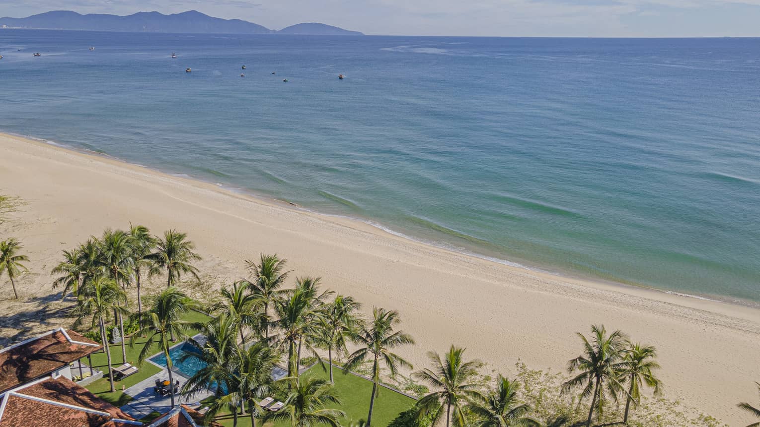Three Bedroom Beachfront Pool Villa aerial shot with ocean and mountain views, palm trees and blue skies