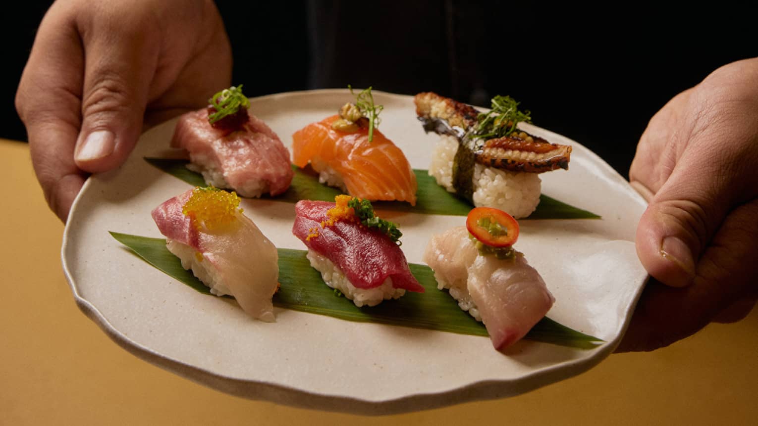 A person in a black shirt holds a plate with six different pieces of sushi.