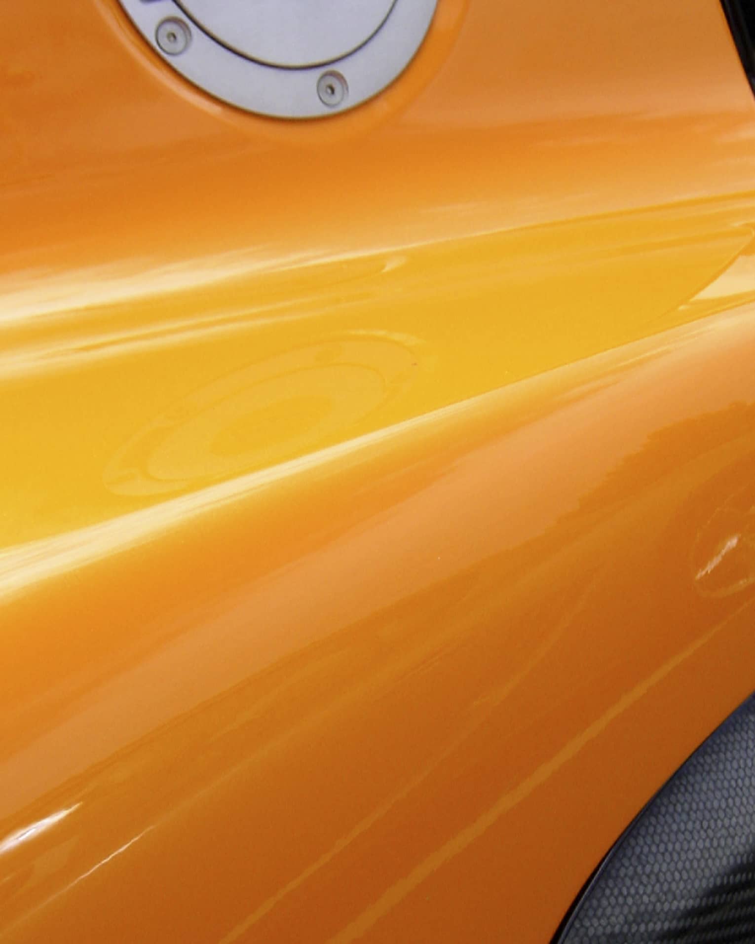 Extreme close-up of the side of a glossy, tangerine orange sportscar with silver and carbon grey accents.