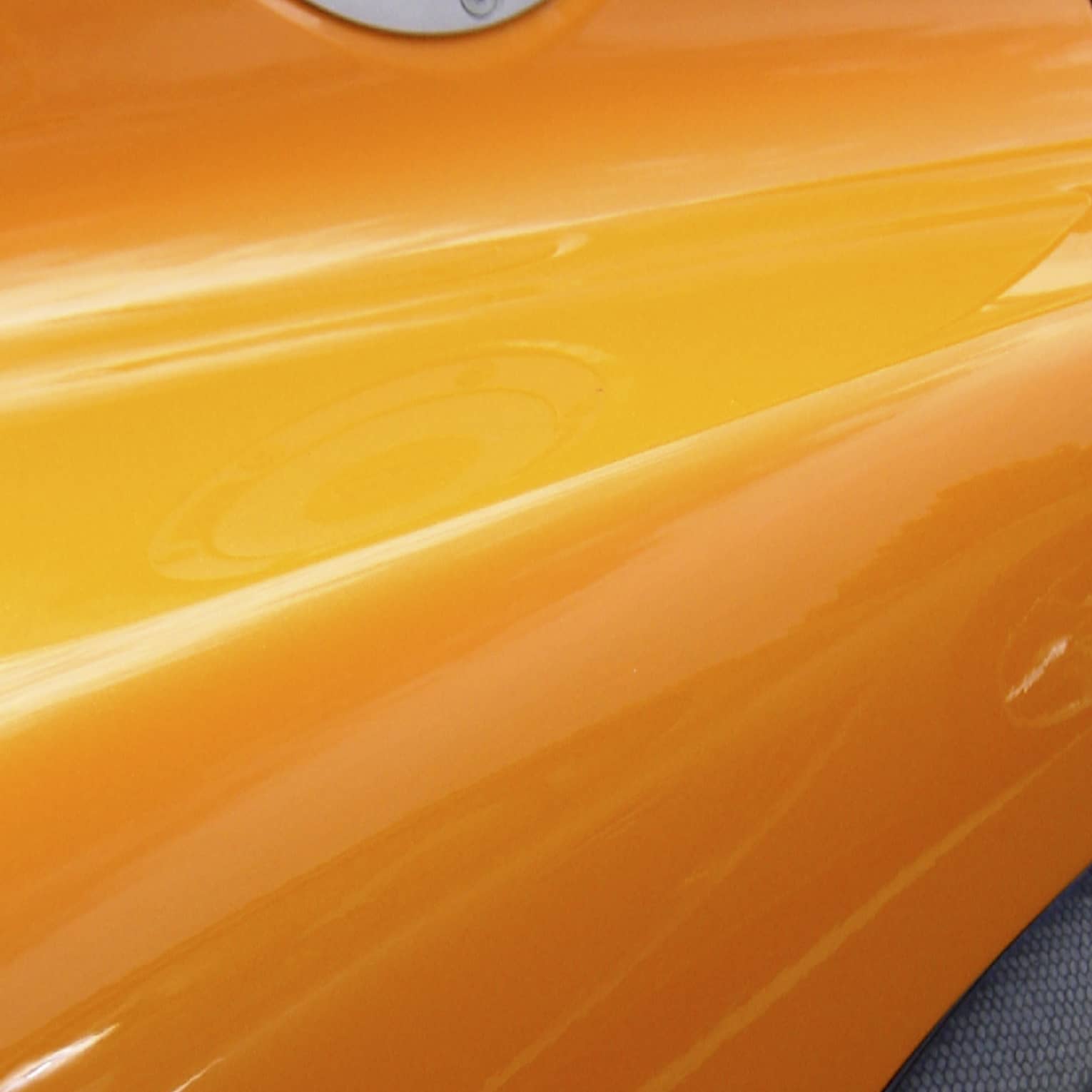Extreme close-up of the side of a glossy, tangerine orange sportscar with silver and carbon grey accents.
