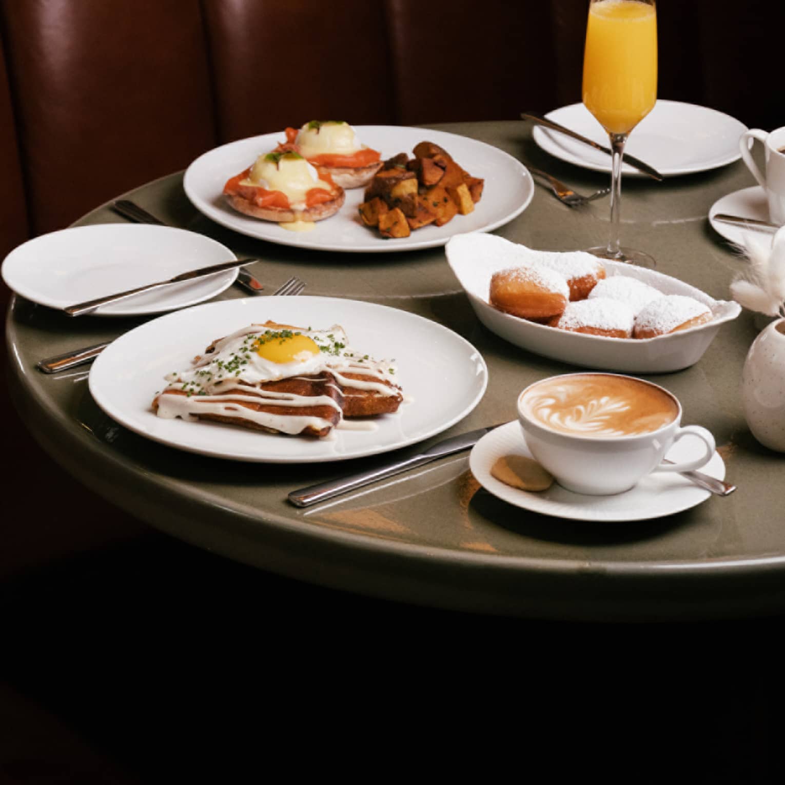 White dishes of brunch dishes and mimosa flute on round grey table