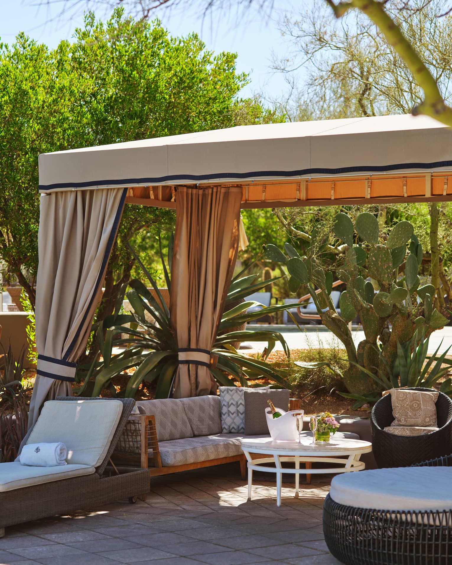 Cabana with lounge chairs, a couch, table and trees surrounding it.