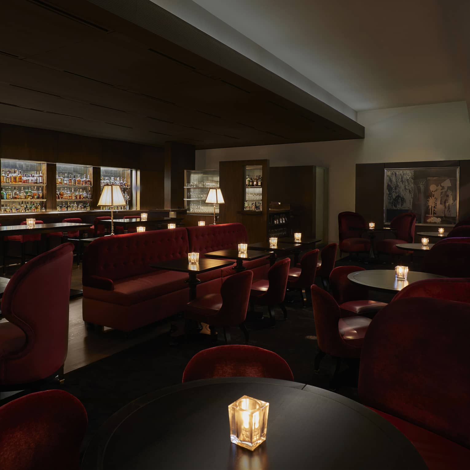 A dimly lit lounge with red chairs and a large selection of drinks behind a bar.