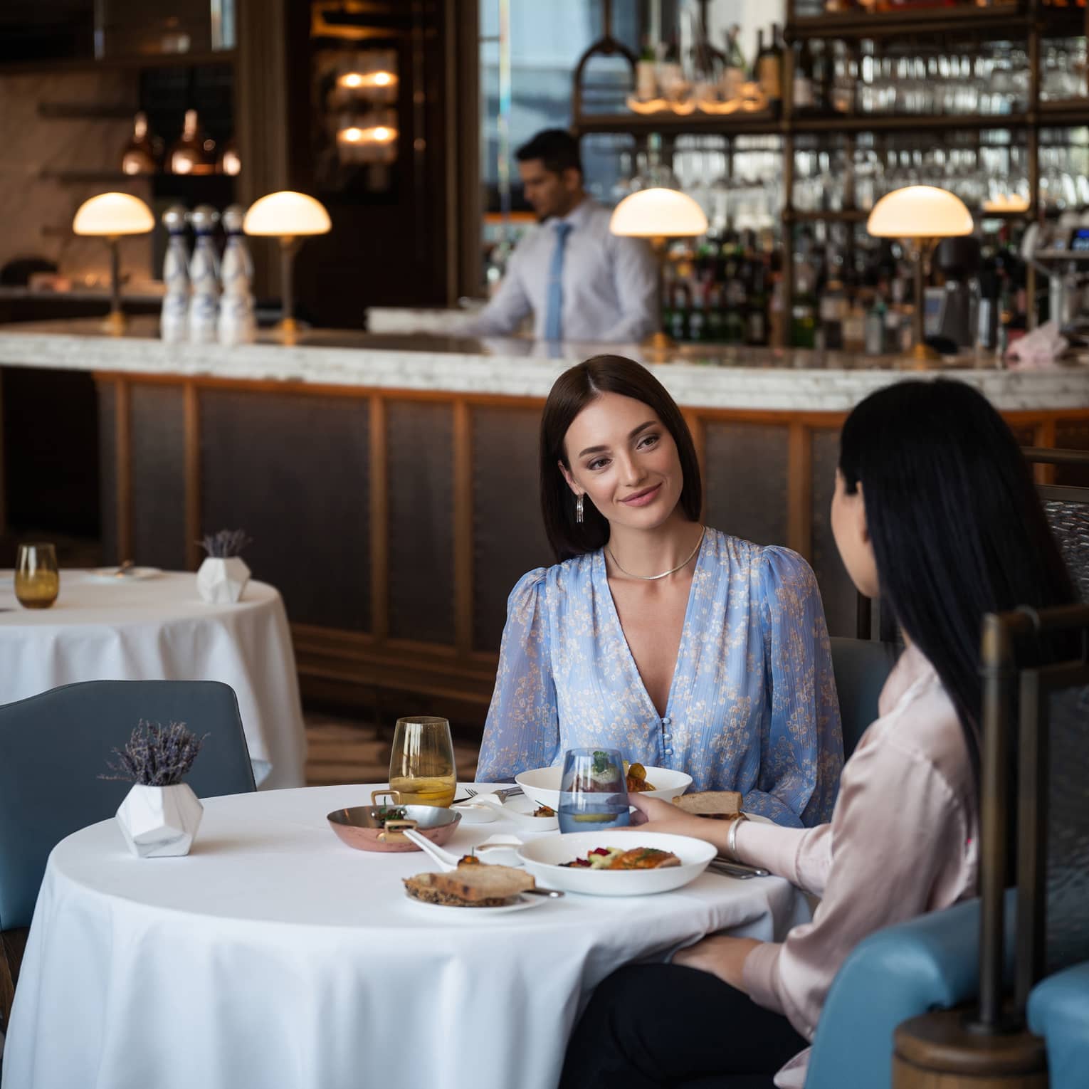Two women sitting at a round dining table in the center of a restaurant