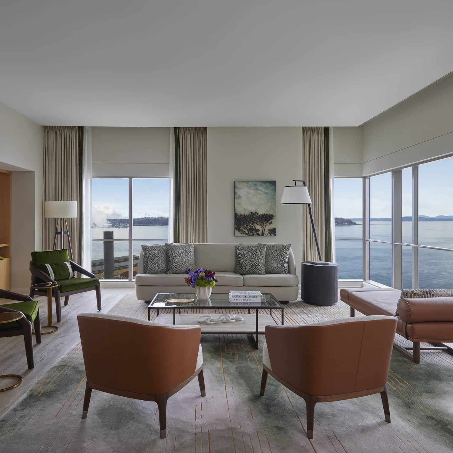 Living room with sofa, four chairs, fireplace and TV, chaise and wrap-around windows looking out to Seattle seafront
