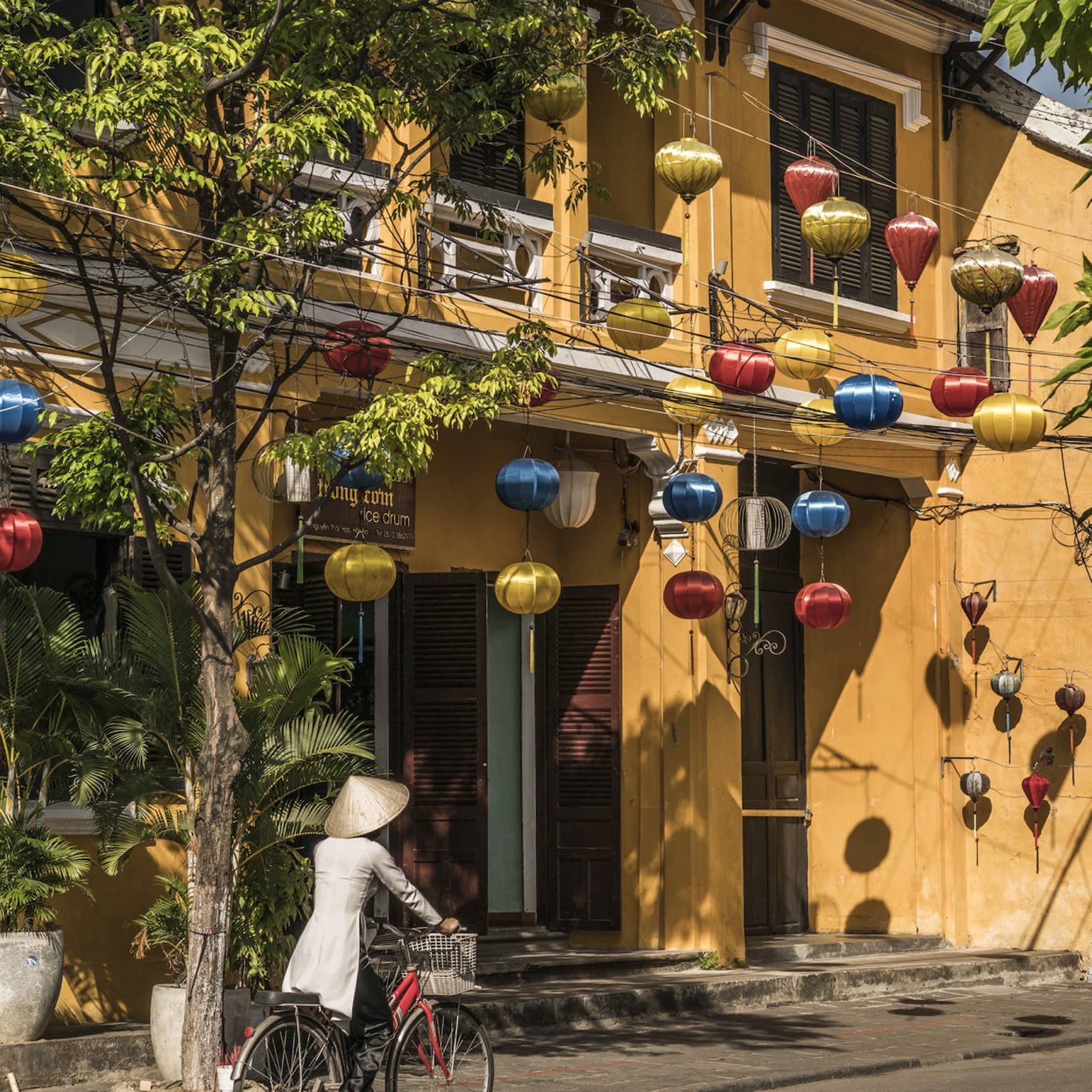 A woman biking down a historic street in Hoi, Viet Nam with lanterns along the side of a house 