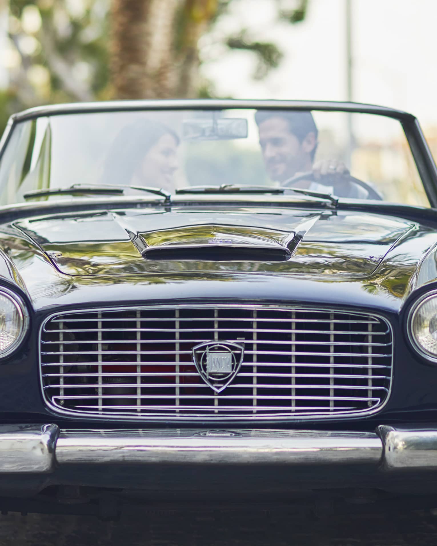 Man and woman sit in black vintage car smiling 