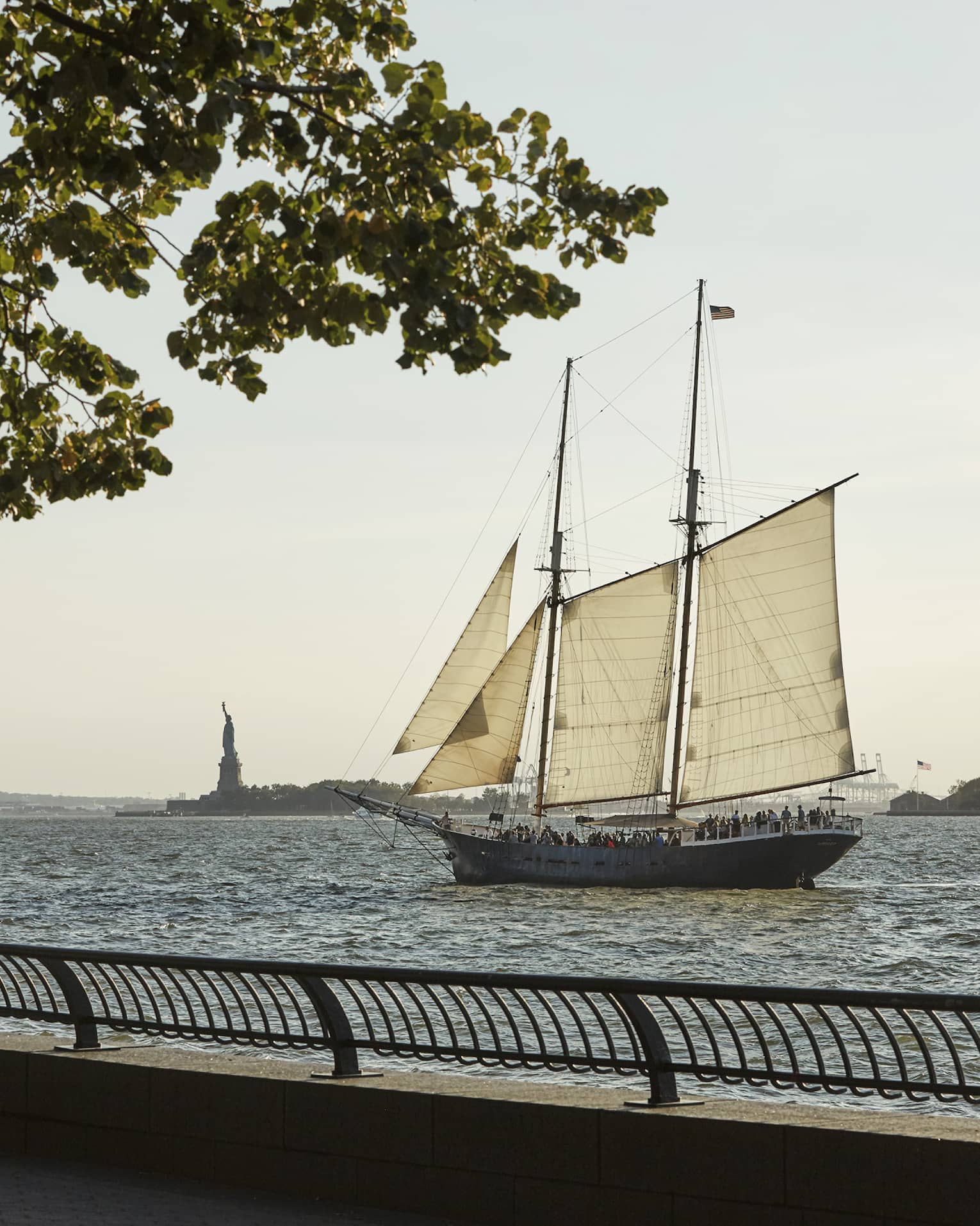 View from boardwalk as sailboat glides past Statue of Liberty in river 