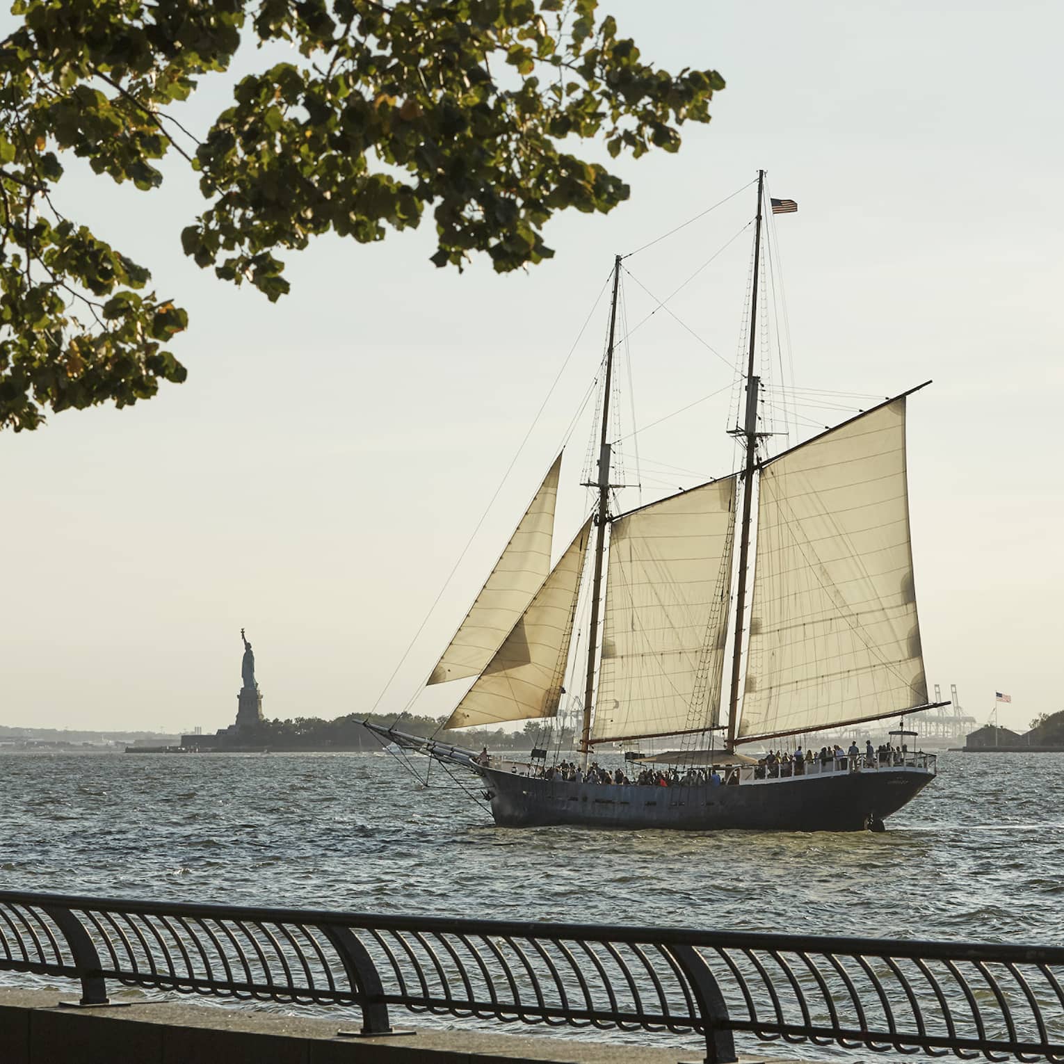 View from boardwalk as sailboat glides past Statue of Liberty in river 