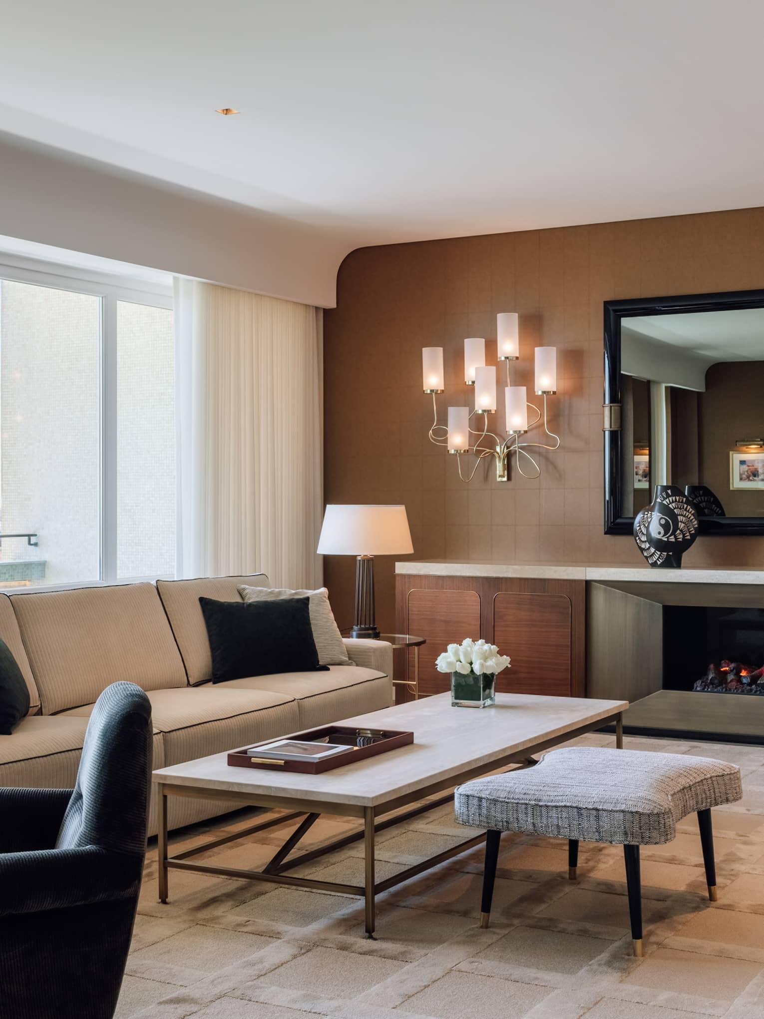 Stylish hotel living room with a sofa, armchairs, coffee table, fireplace and large windows with a city view.