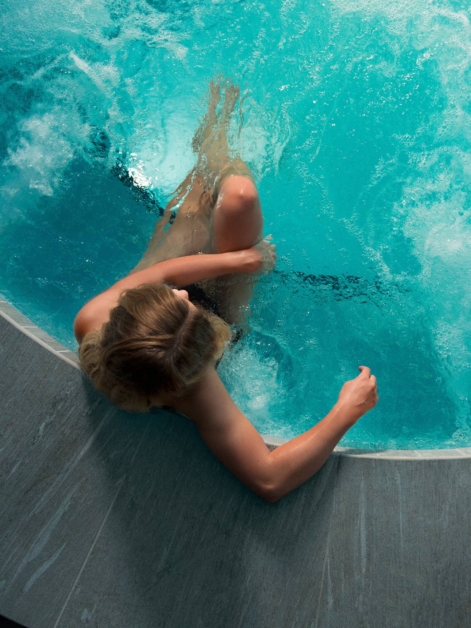 Looking down at woman sitting in round hot tub with blue water