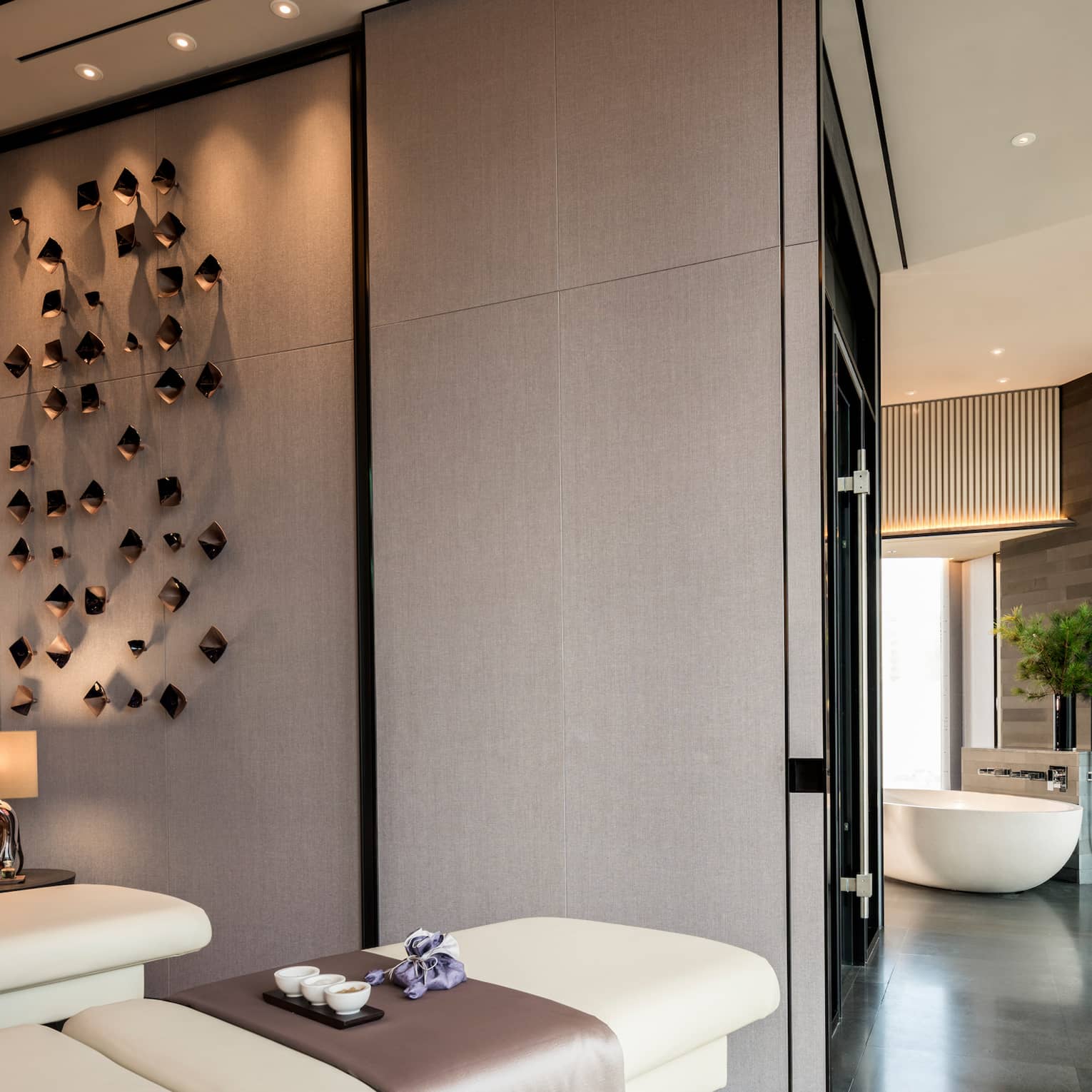 Couples massage beds under modern wall sculptures by hall leading to spa tub