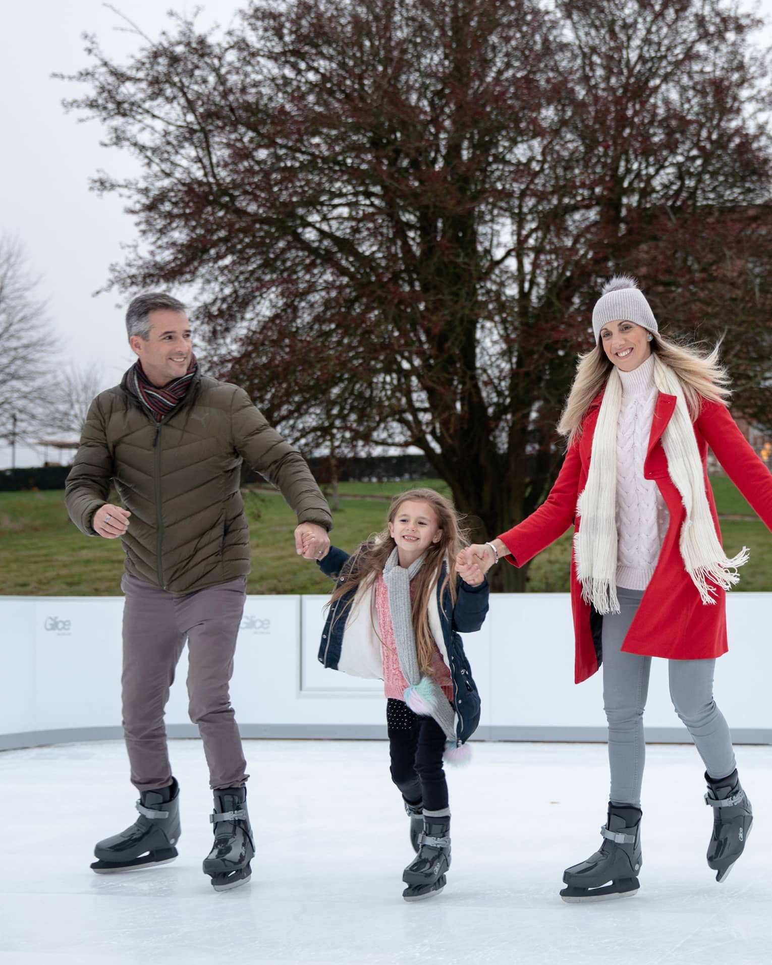 Man and woman holding hands of young girl while ice skating on outdoor rink