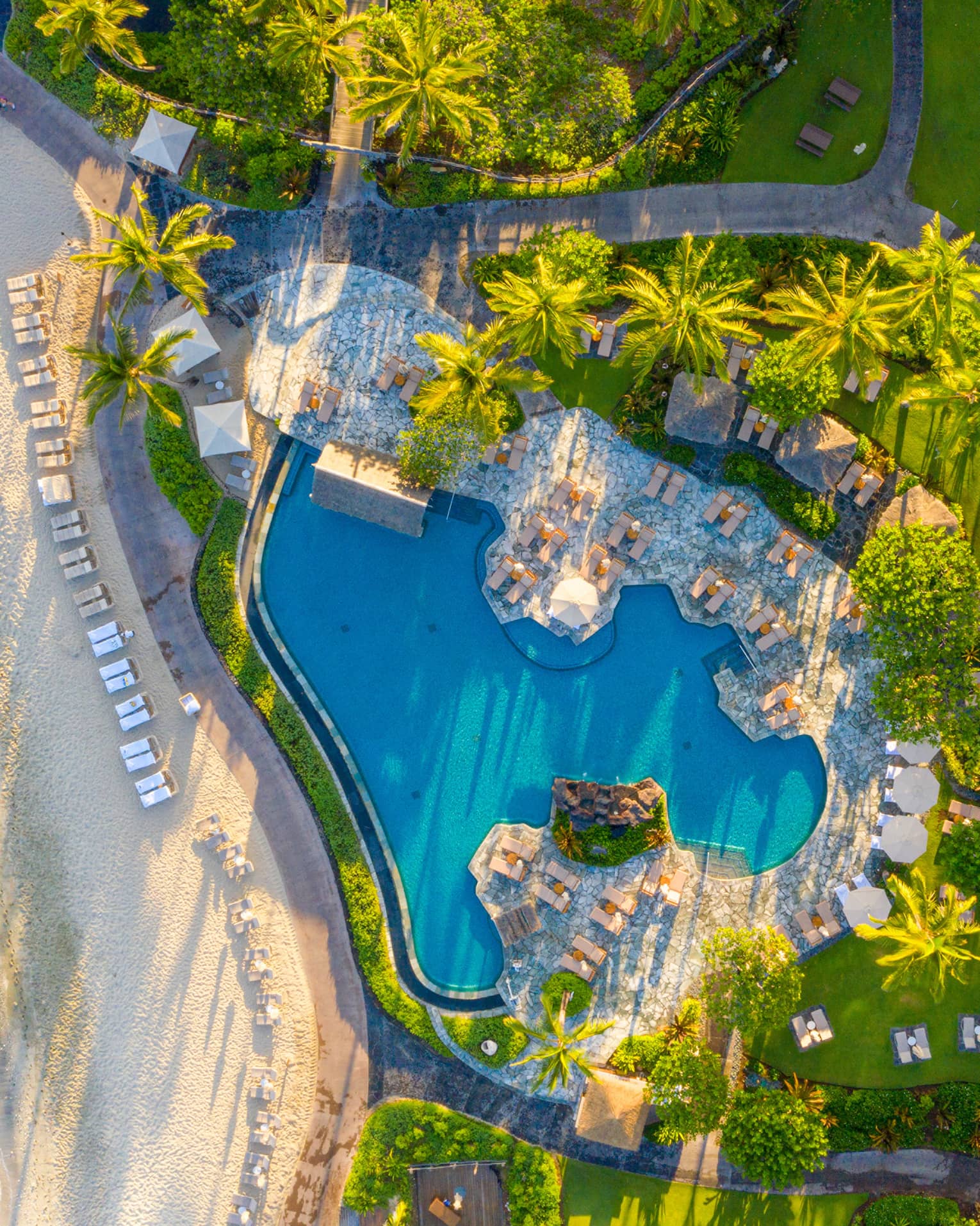 Aerial view of tropical resort pool next to a white-sand beach