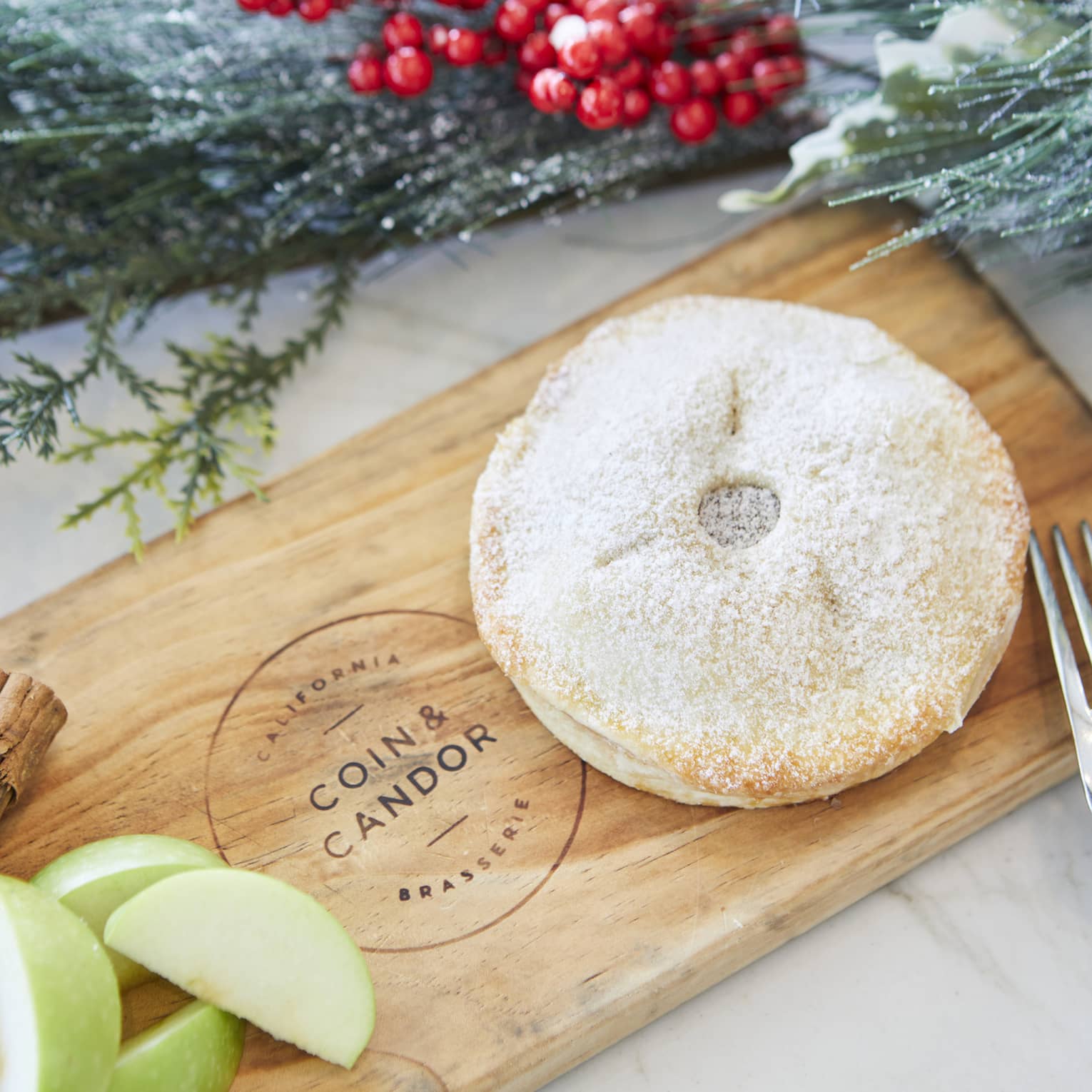 Miniature pie served on a wooden board next to sliced green apples and cinnamon sticks