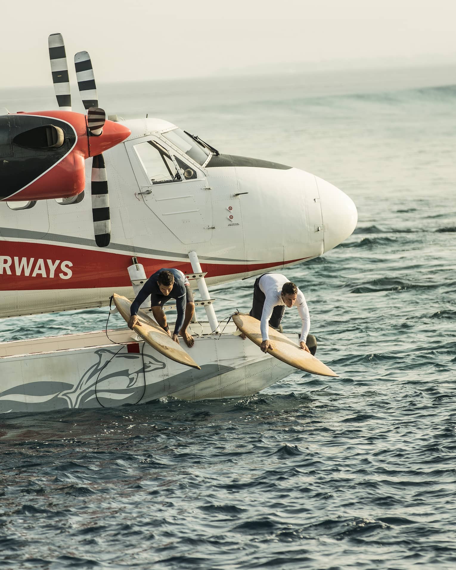 Two people with surfboards jump from float plane onto waves