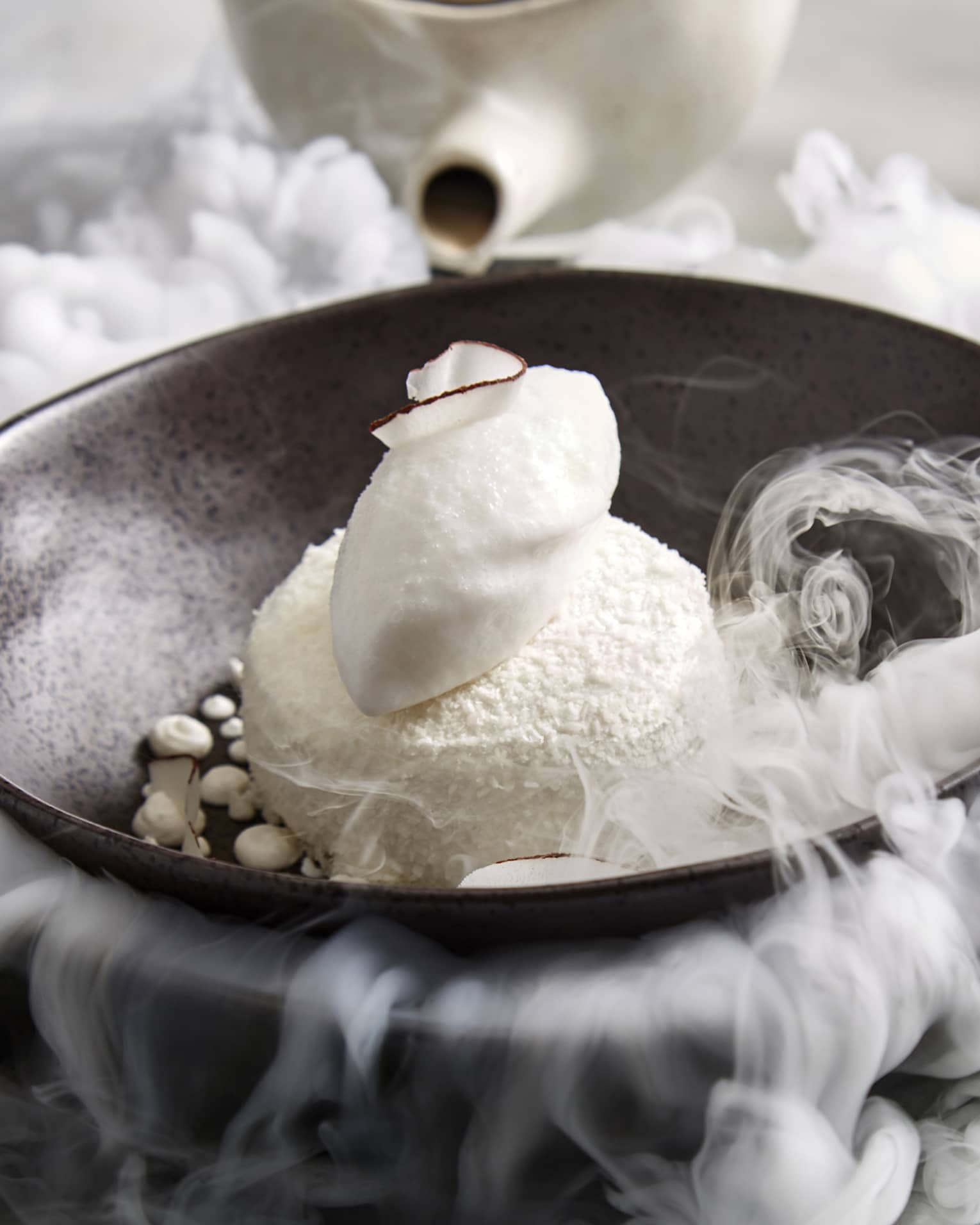 Pavlova served with dry ice on a dark brown plate