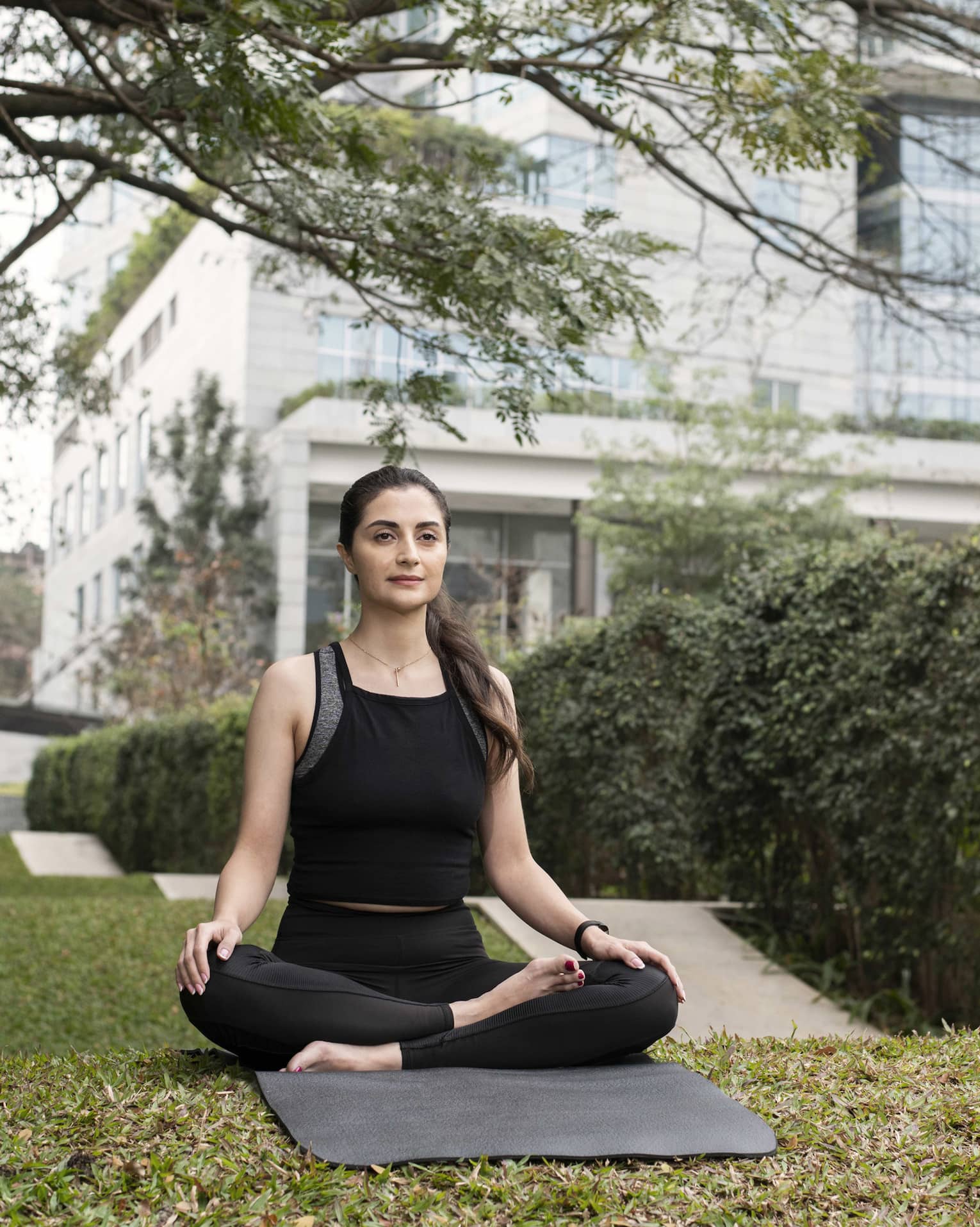 Person wearing athletic clothes and sitting on a yoga mat with their legs crossed.