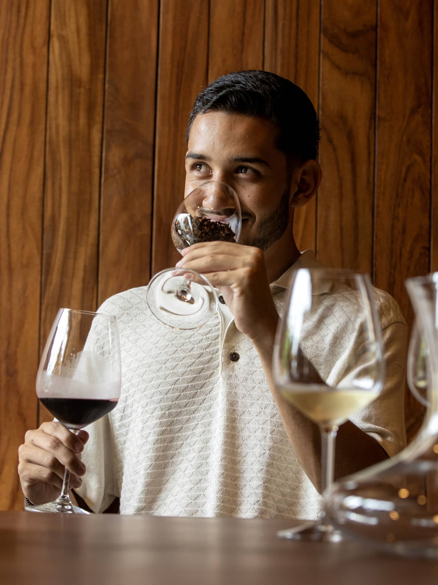 At a wine tasting, a guest smells coffee beans in a glass before tasting the glass of dark red wine held in his other hand. 