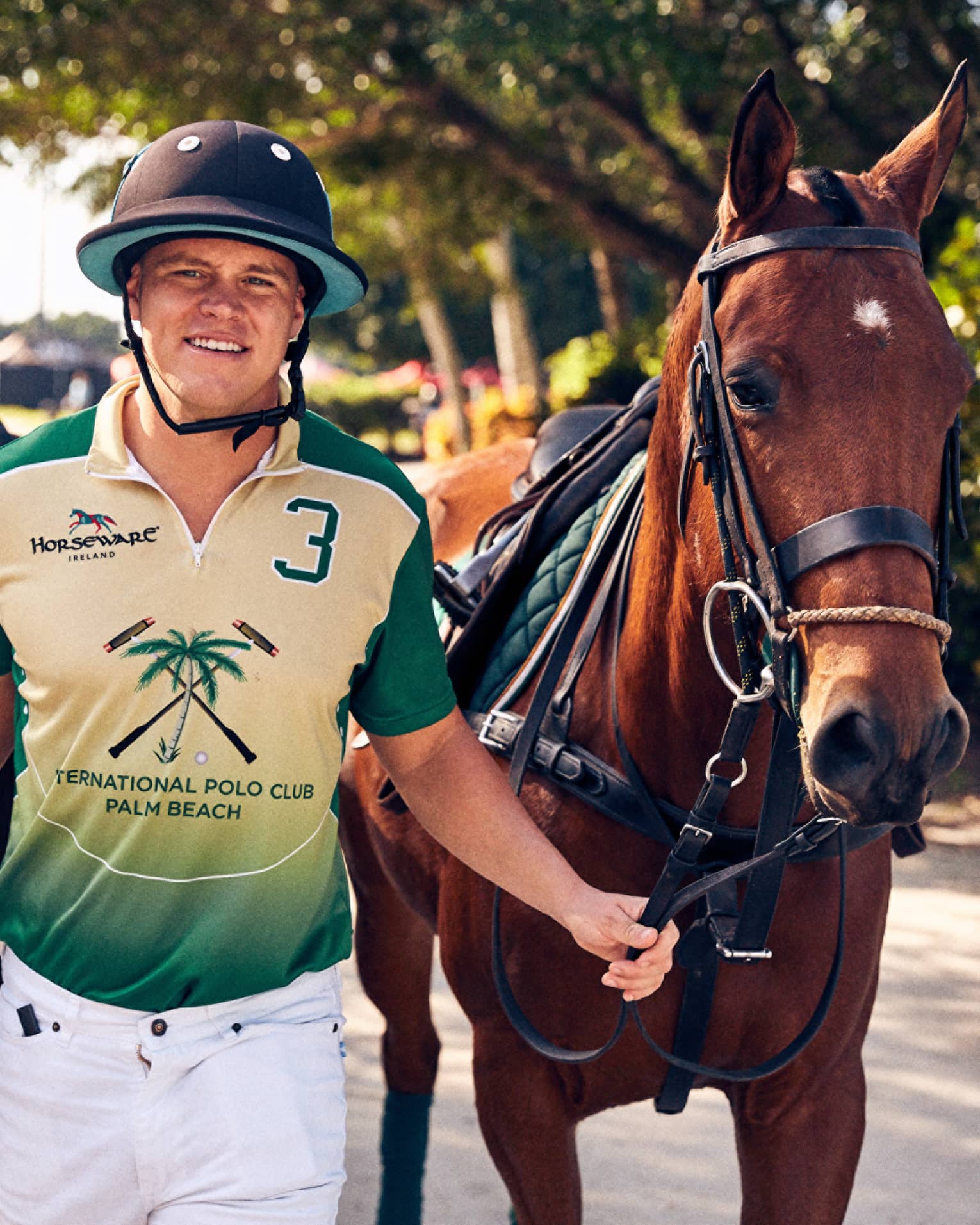A man in a green shirt and helmet is leading two horses.