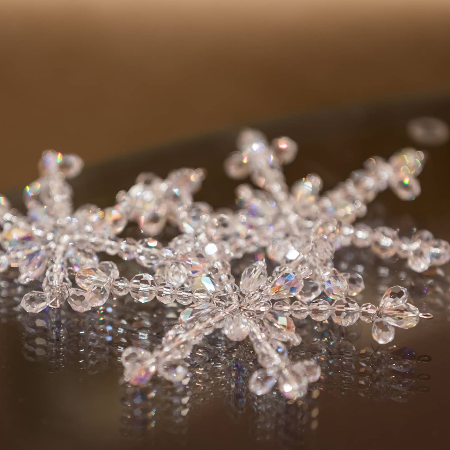 Three snowflake ornaments made of crystal beads placed on a dark table