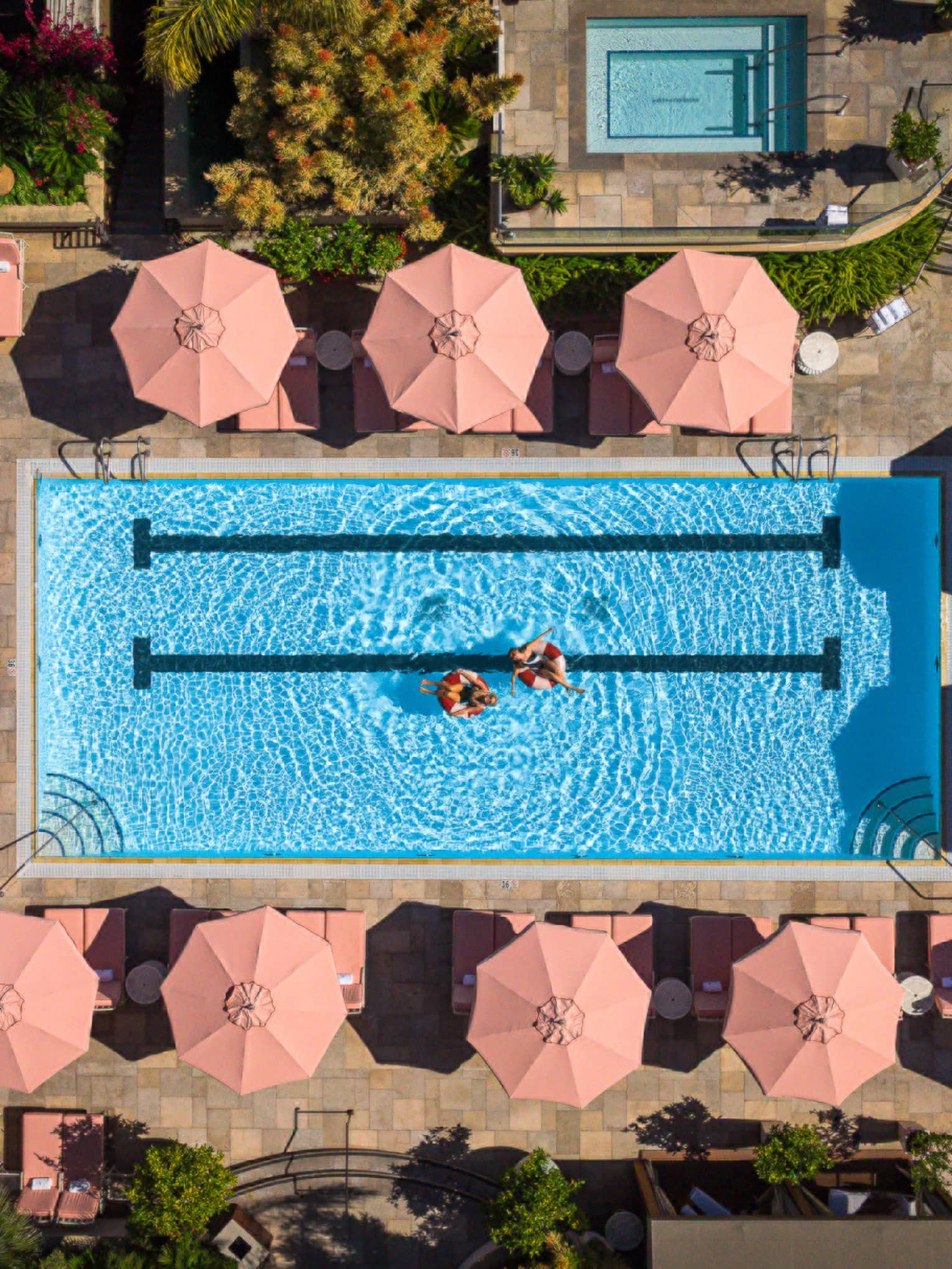 Aerial view of luxury hotel pool surrounded by pink umbrellas and lounge chairs