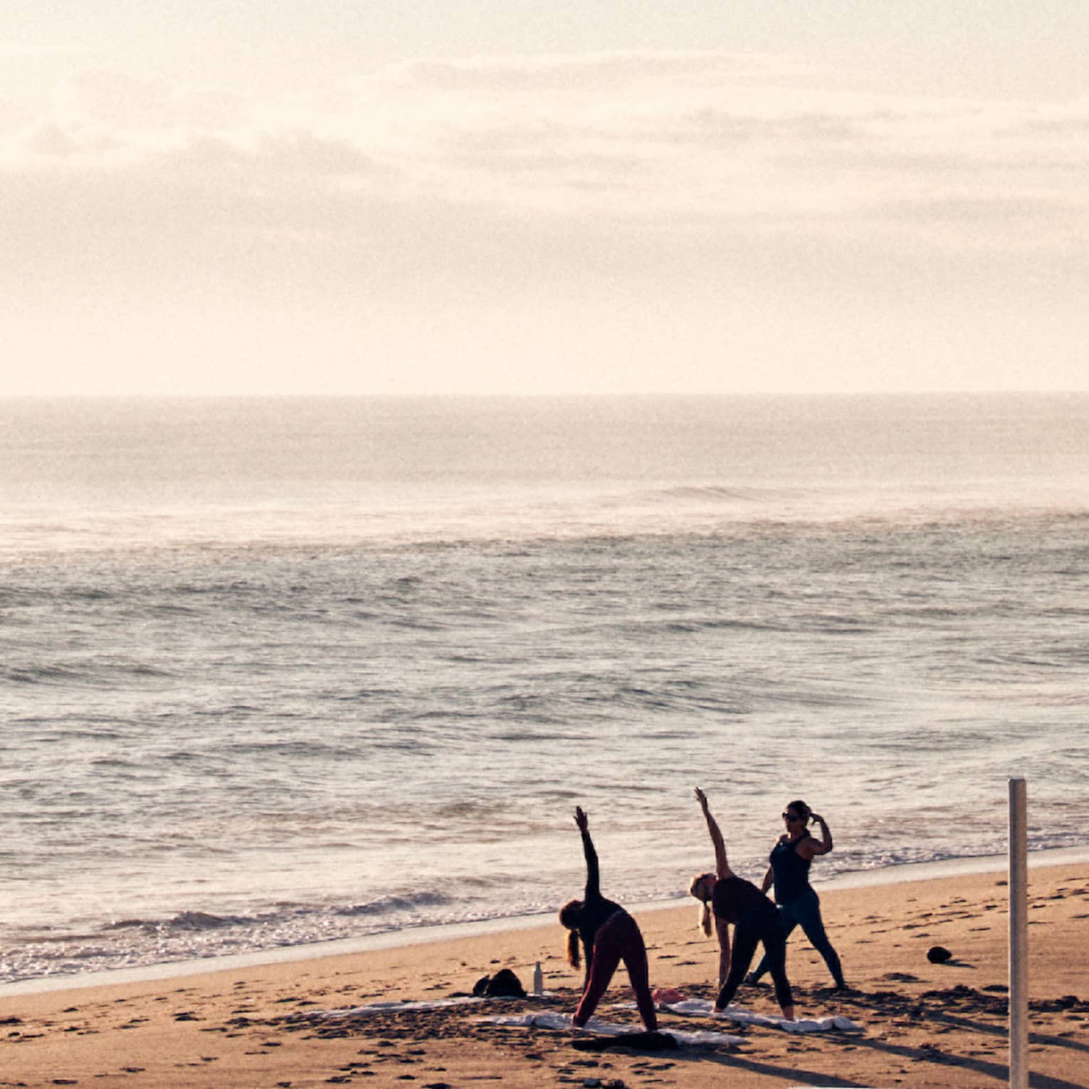Three guests doing yoga on the shore of the beach with the ocean in the background.