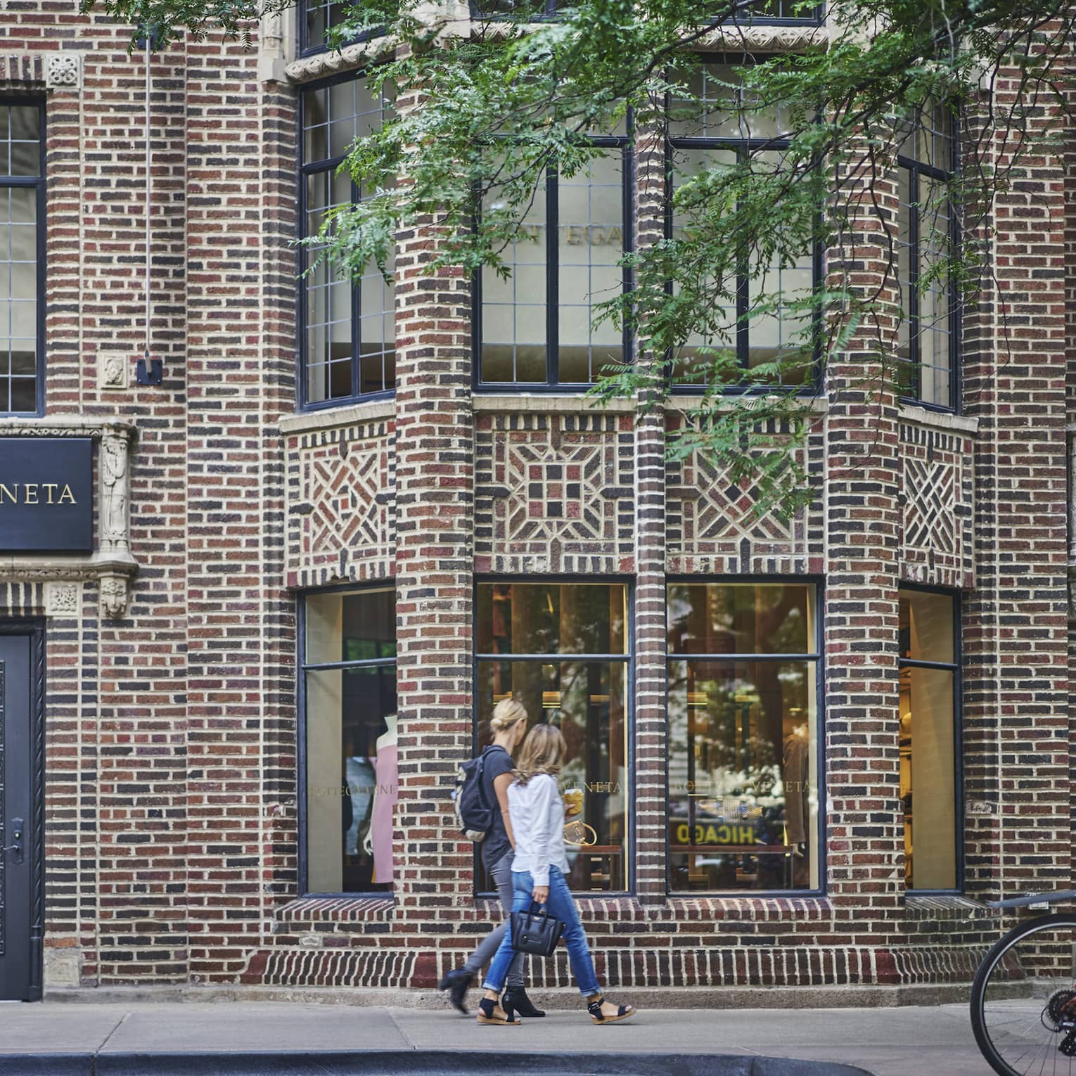 Two people walking down a street with brick buildings.