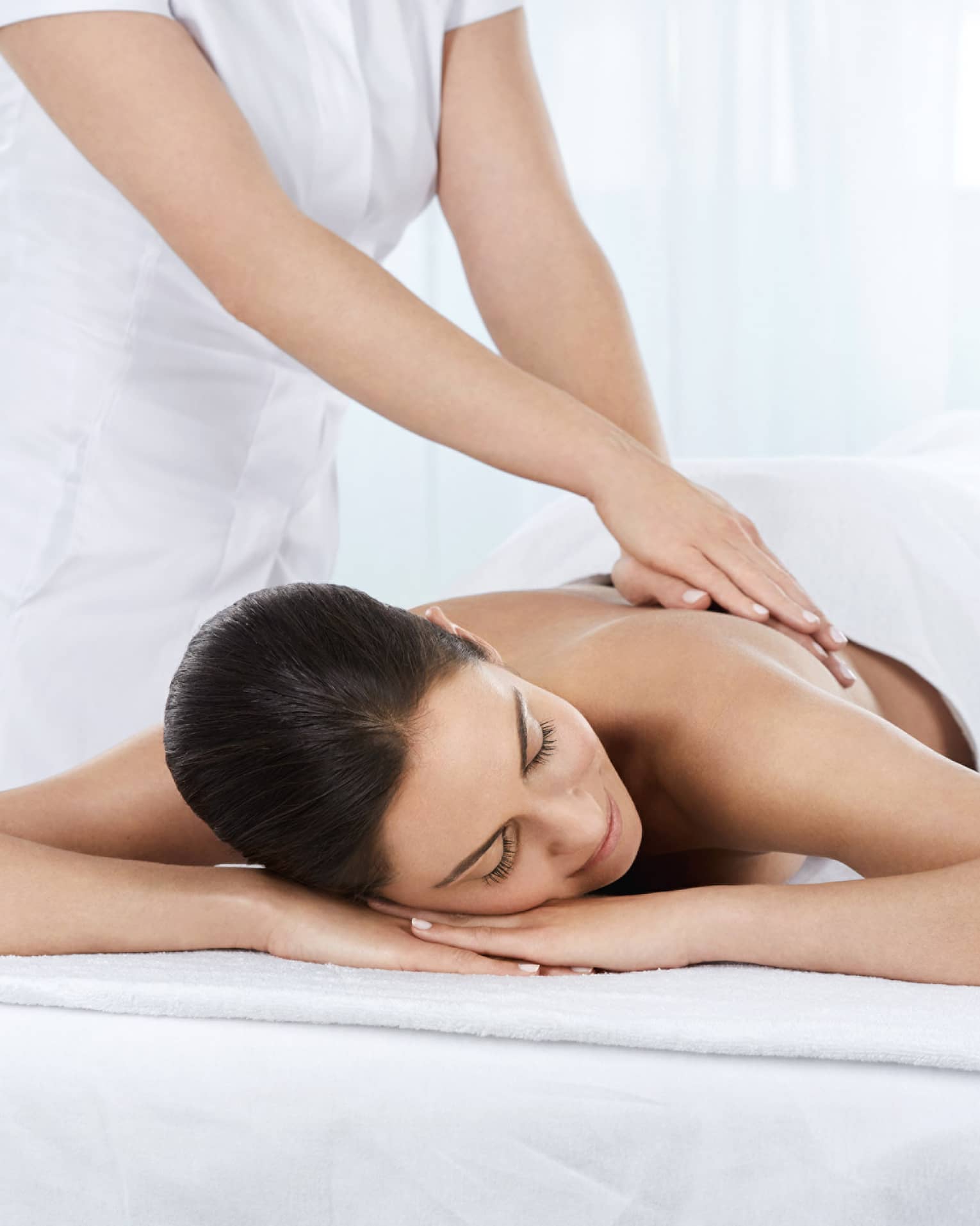 Woman lies under white sheet on massage table as hands massage her bare back