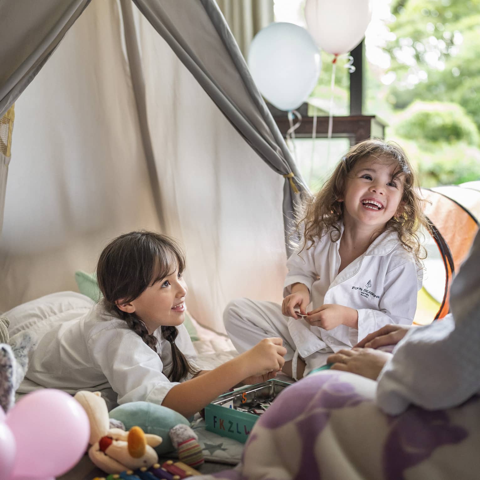 Two children in Four Seasons pajamas, smiling and playing together in a cozy indoor tent setup