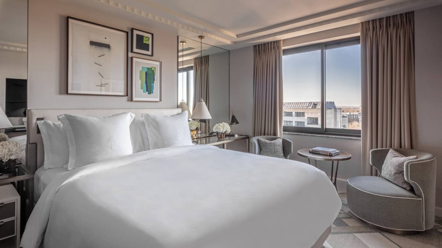 ,Superior Room at Four Seasons London Park Lane in Mayfair, offering a blend of comfort and luxury. The room features a large, king-sized bed covered in crisp white linens, surrounded by tasteful decor, including muted gray curtains, elegant lamps and a selection of framed artworks on the walls. A comfortable seating area by the window provides a relaxing space with a curved armchair and a small table, perfect for enjoying the city views. The room's modern and understated elegance is emphasized by its clean lines and soft colour palette.