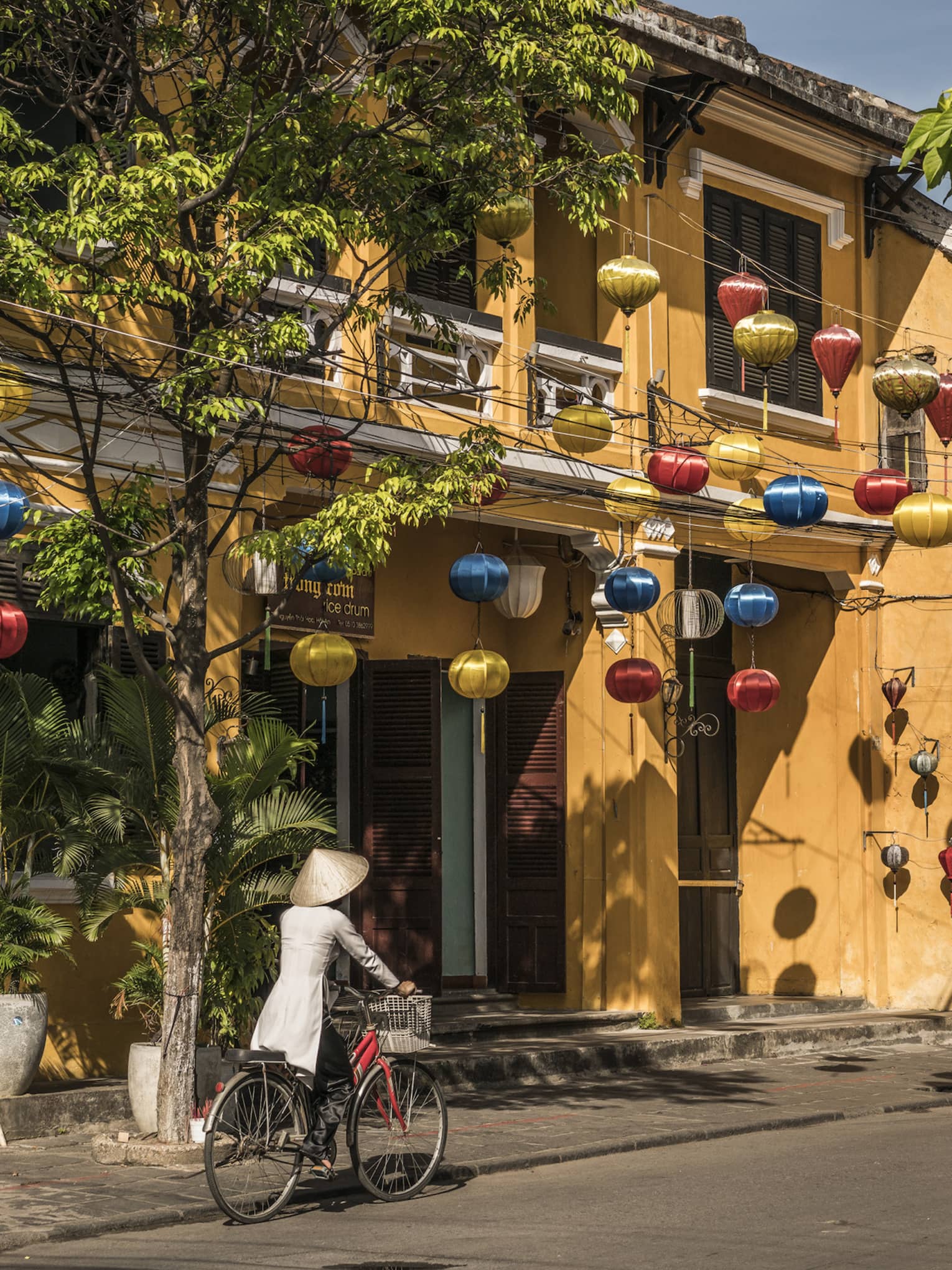 A woman biking down a historic street in Hoi, Viet Nam with lanterns along the side of a house
