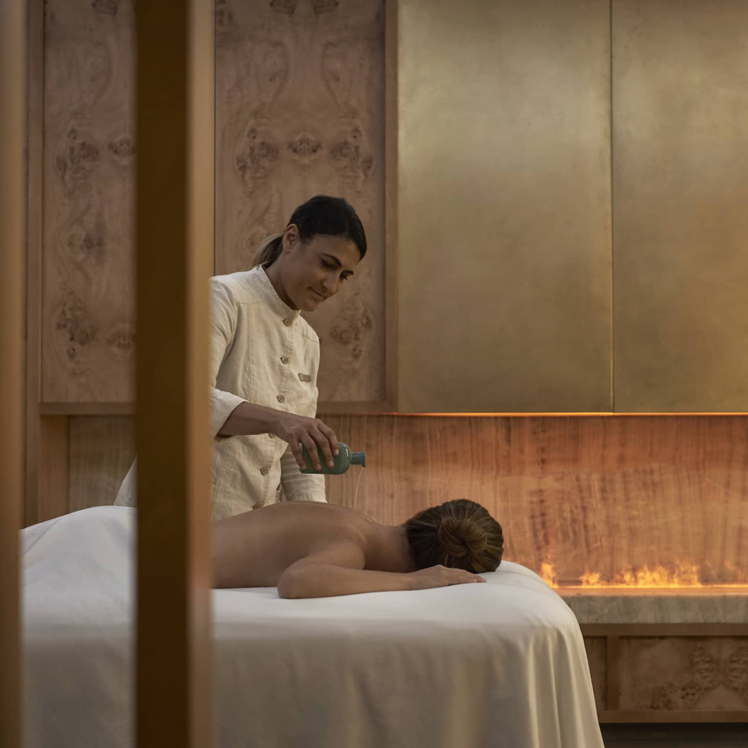 Spa therapist pours oil on back of person facedown on spa table