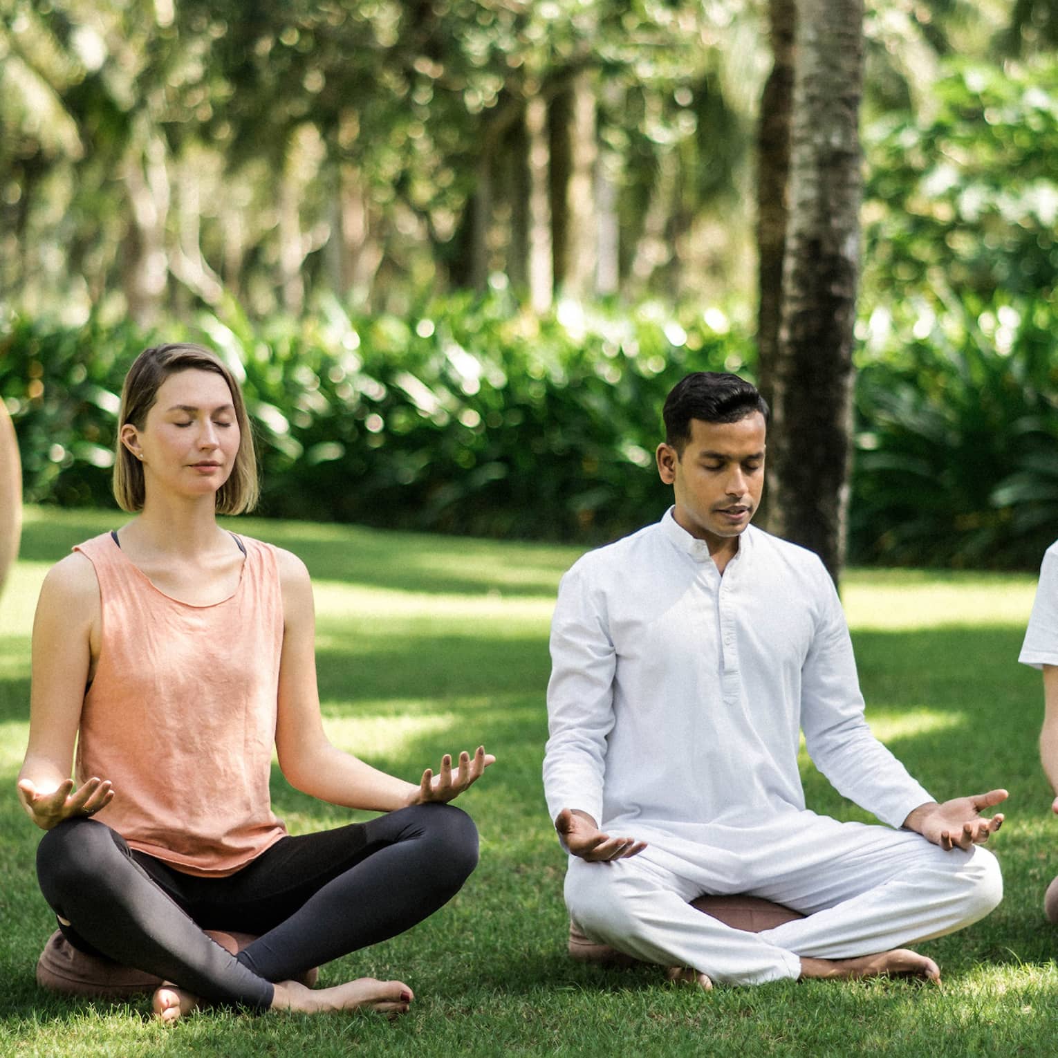 Two men and a woman practise meditation yoga outdoors on lawn