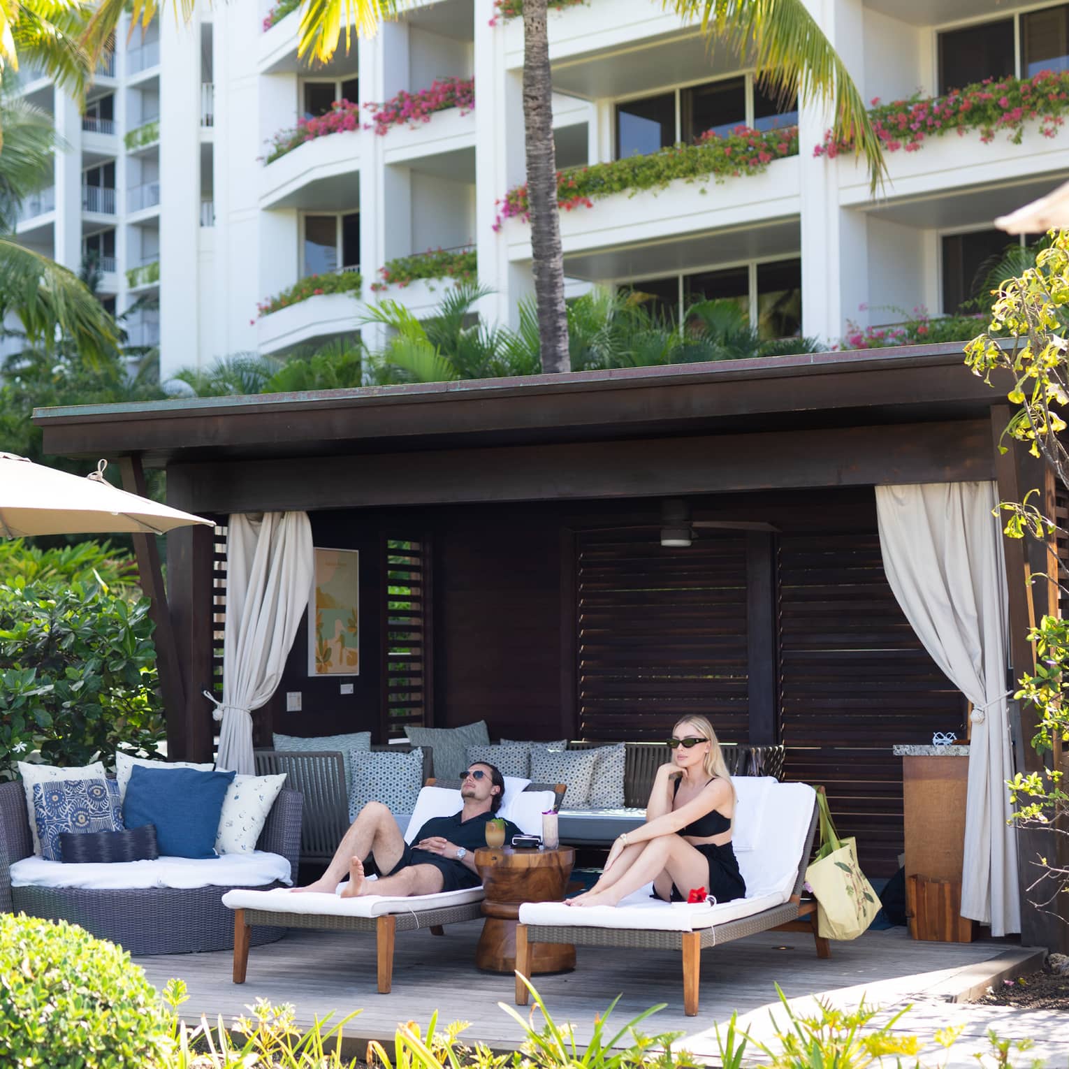 Man and woman lounge on sun chairs under private cabana