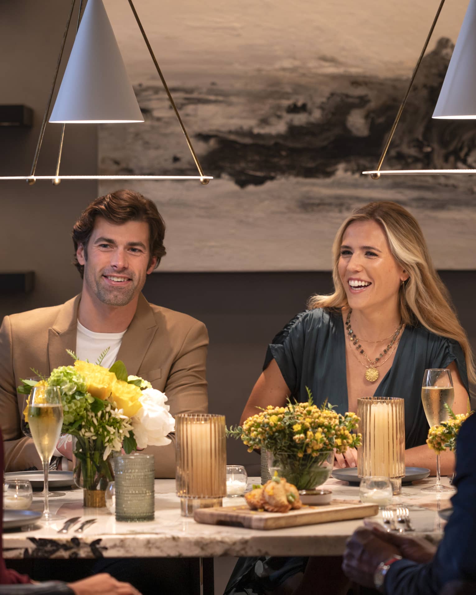 Guests sitting at a table and smiling at each other at a restaurant with overhead lighting