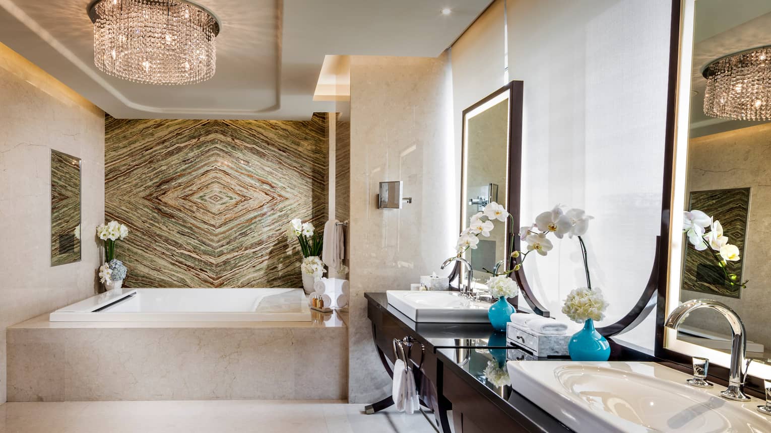 The Imperial Suite’s luxurious bathroom with two sinks and a large bathtub lit by an ornate chandelier.  