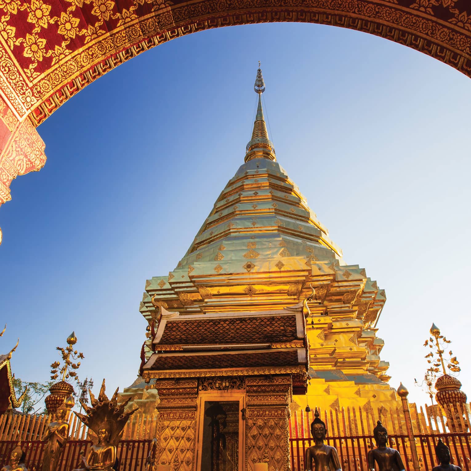 View from under painted arch looking up at golden Wat Phra That Doi Suthep historic Buddhist temple, statues 