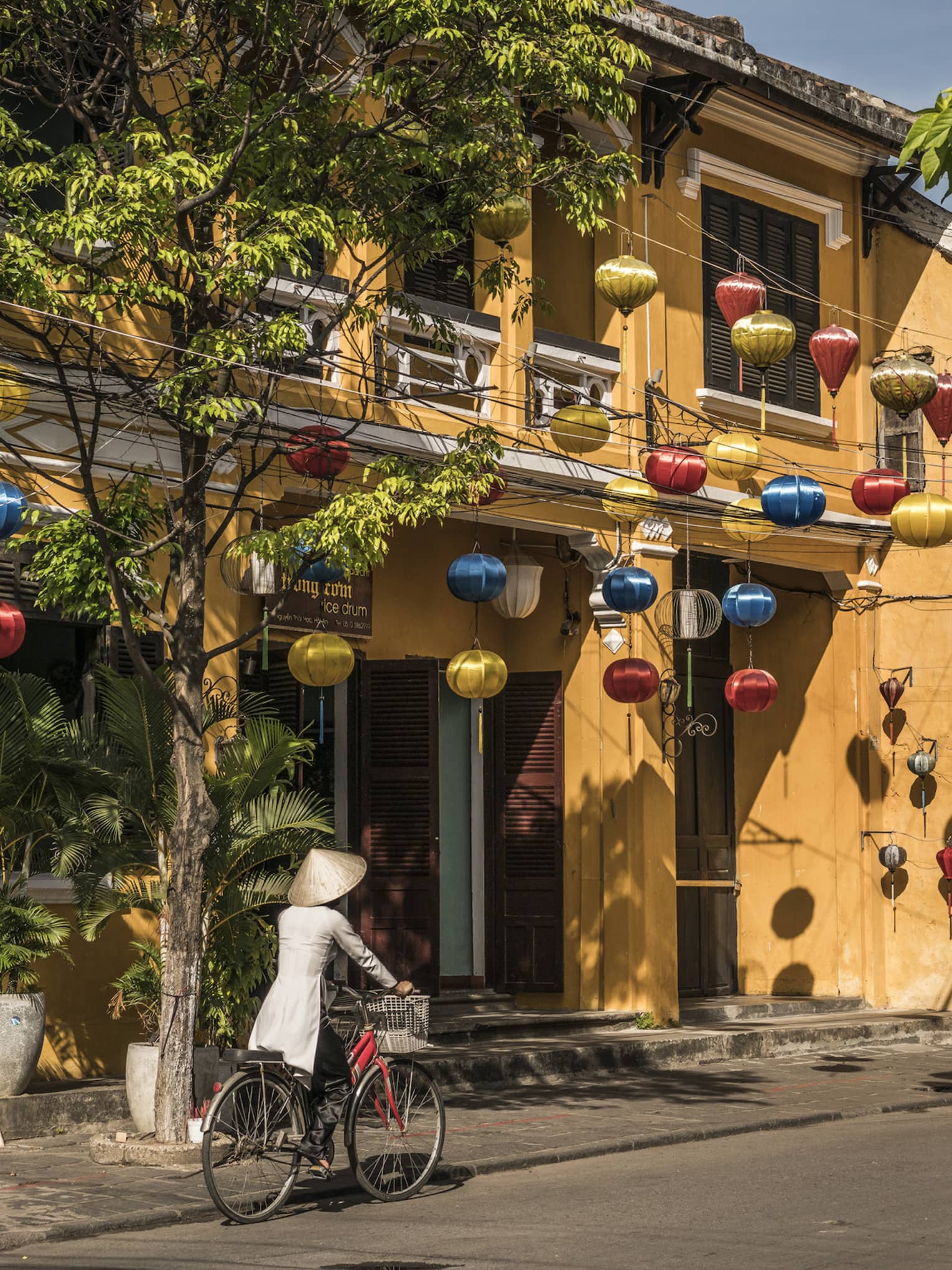 A woman biking down a historic street in Hoi, Viet Nam with lanterns along the side of a house 